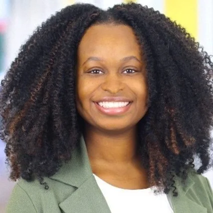Portrait of a smiling woman with curly hair, wearing a green blazer and a white top.