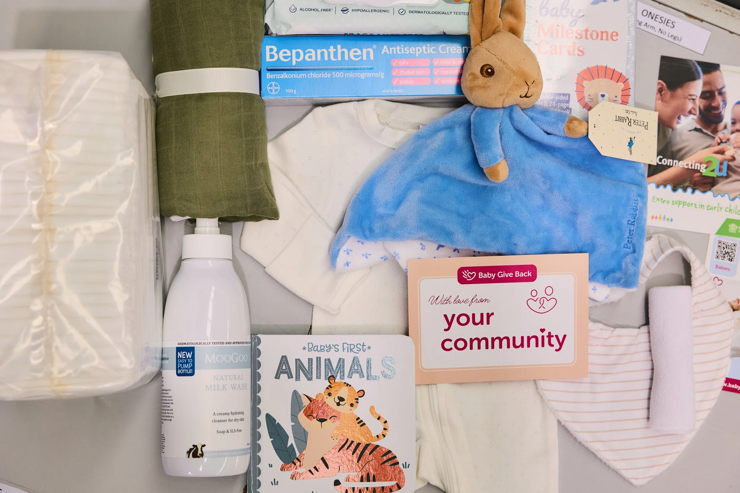 flat lay of baby items, onesie, wrap, nappies, book and a toy