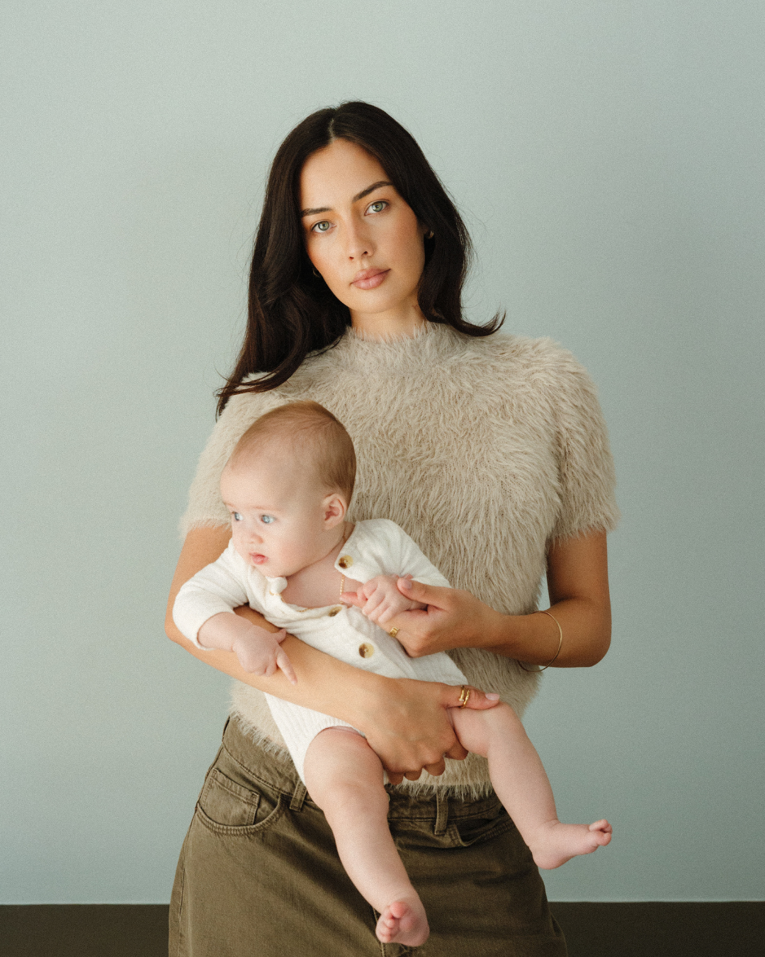 Natural light studio shot of a mother and baby against a light blue backdrop 