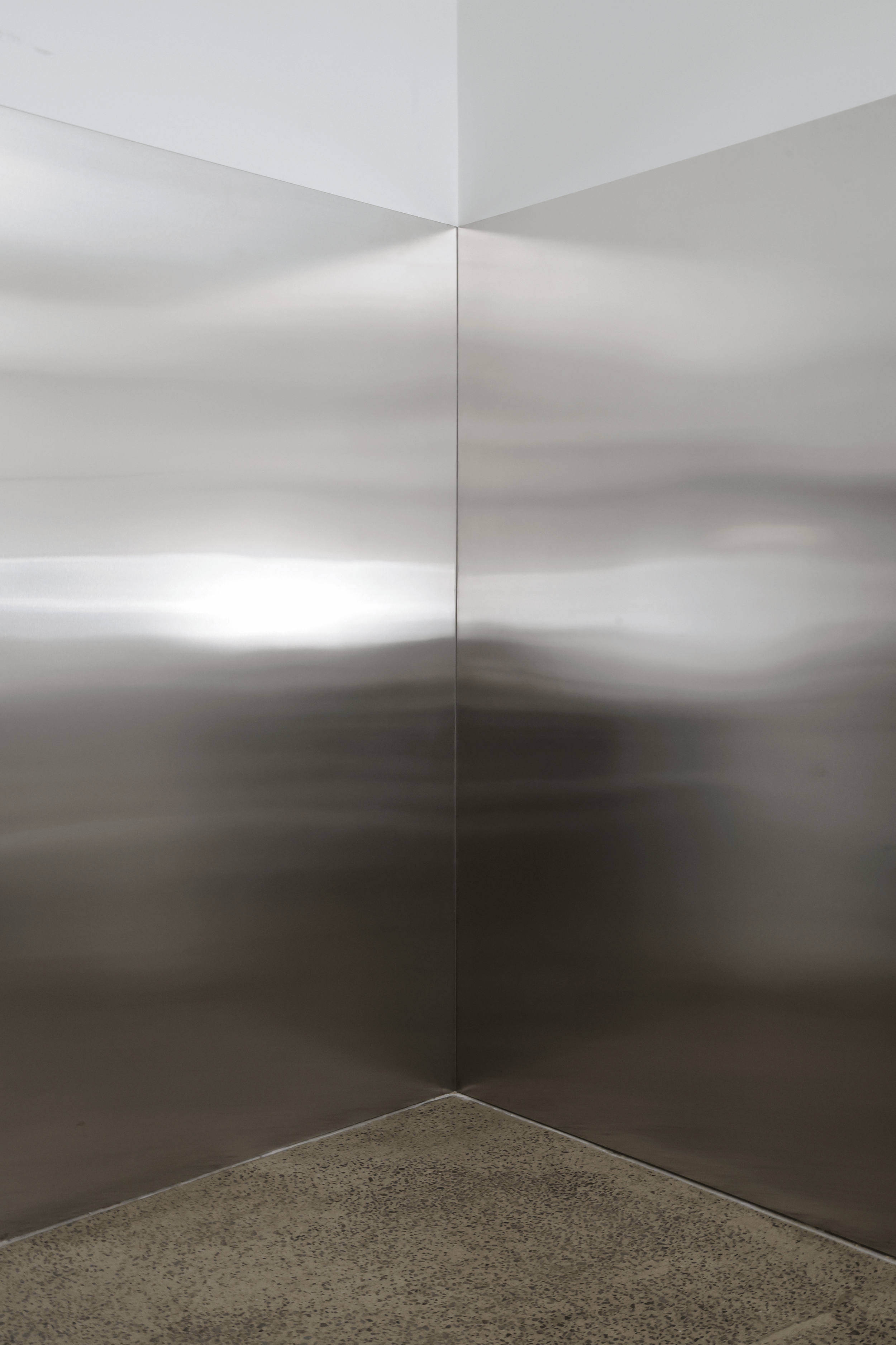 Corner of an elevator with stainless steel walls and a speckled floor.