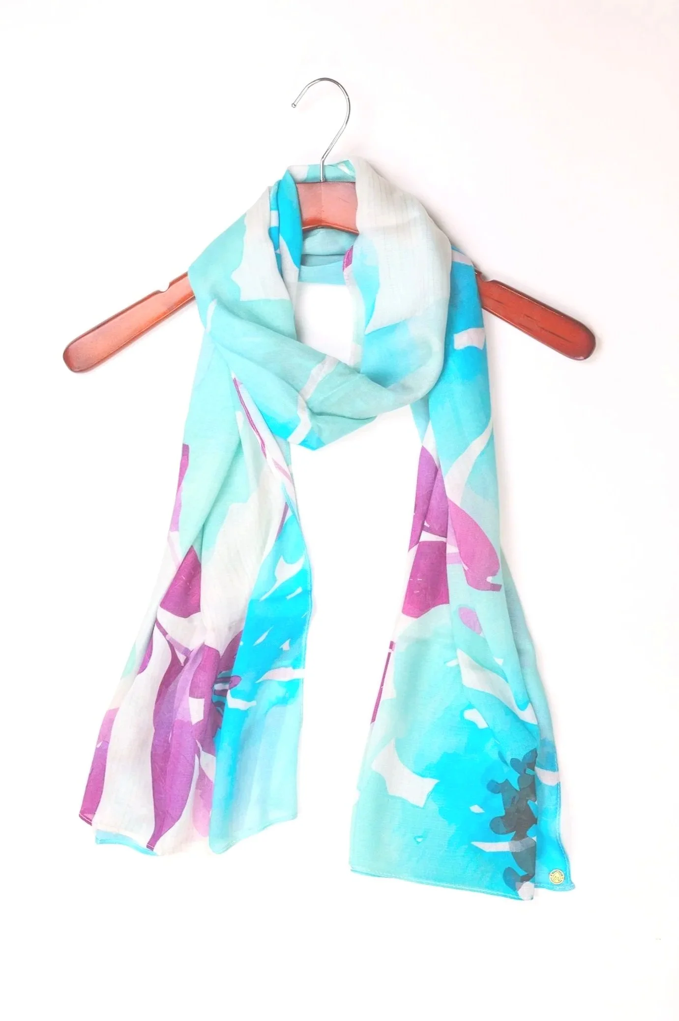 Colorful scarf hanging on a pink hanger on a wooden stick against a white background.