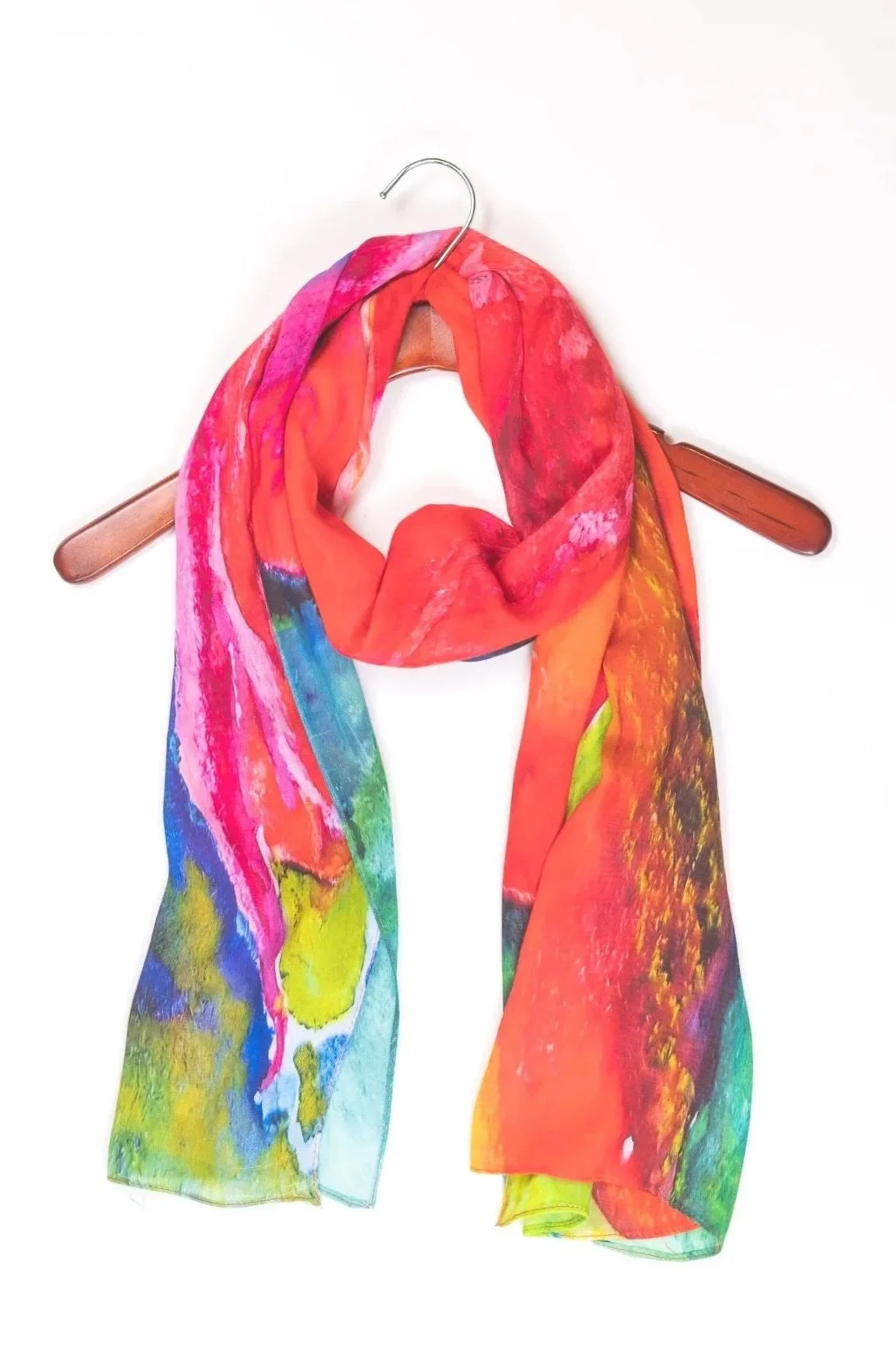 Colorful scarf with abstract watercolor pattern hanging on a wooden hanger against a white background.