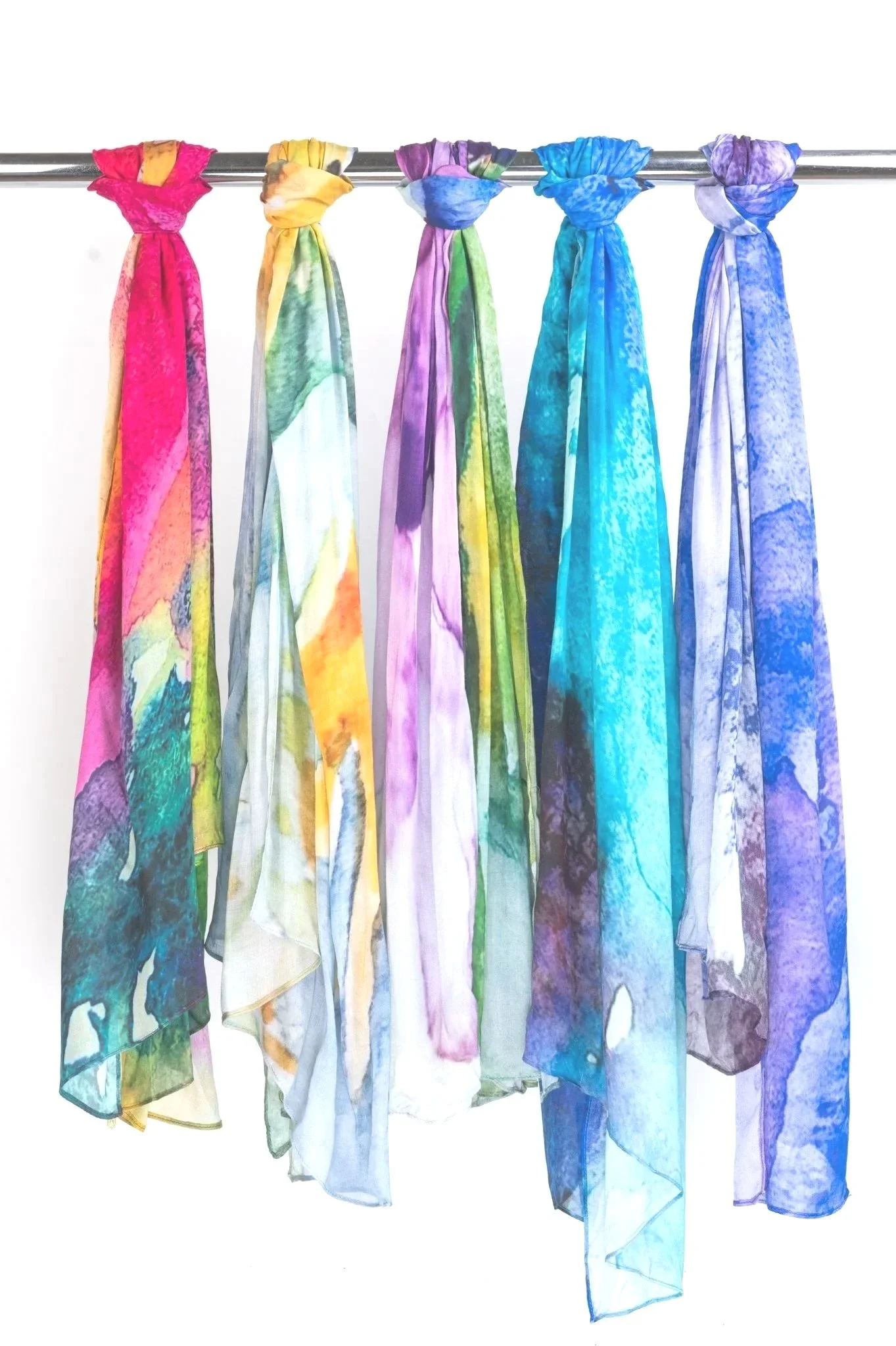 Six colorful scarves hanging on a metal rod, arranged in a rainbow pattern from pink to purple.