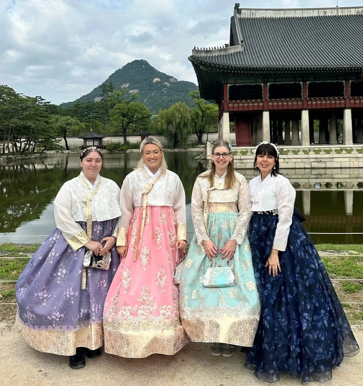 Group of solo female travellers wearing traditional Korean hanbok outside a temple by a lake in South Korea.