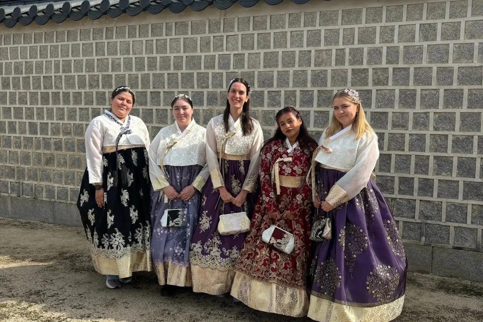 Group of solo female travellers wearing traditional Korean hanbok dresses, standing by a historic wall in South Korea.