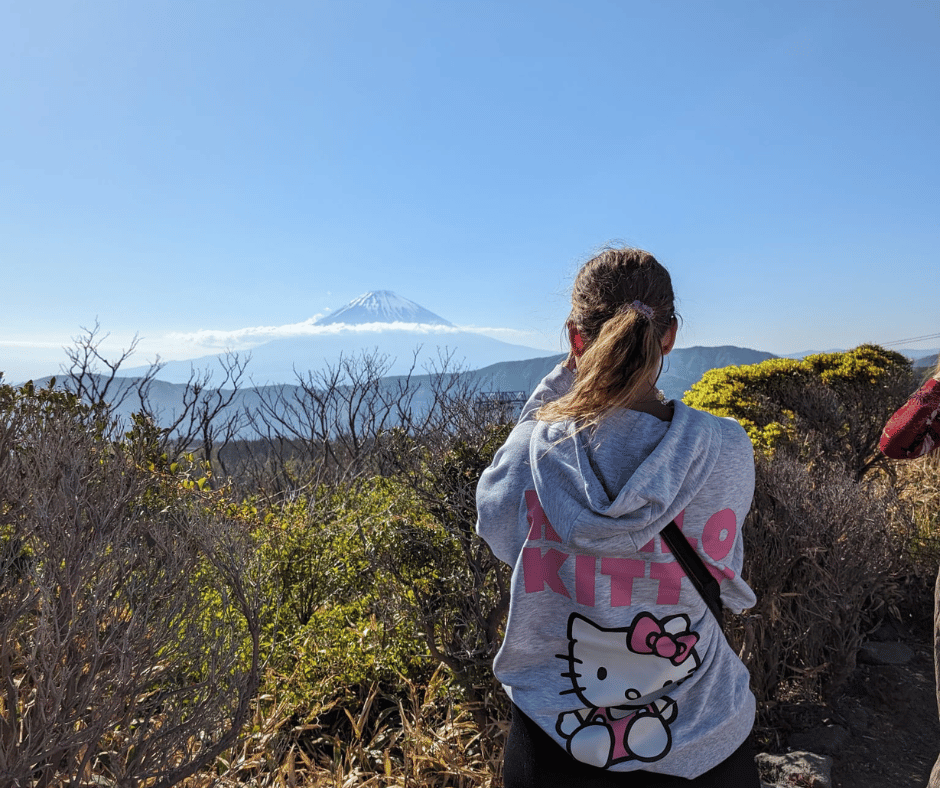 Solo female traveller taking a photo of Mount Fuji during cherry blossom season in Japan.