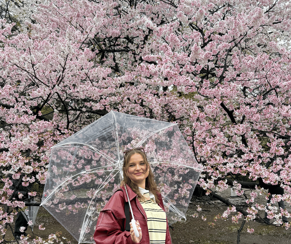 Gabi standing in front of a cherry blossom tree in Japan during sakura season, showcasing a safe and beautiful destination for solo female travellers.