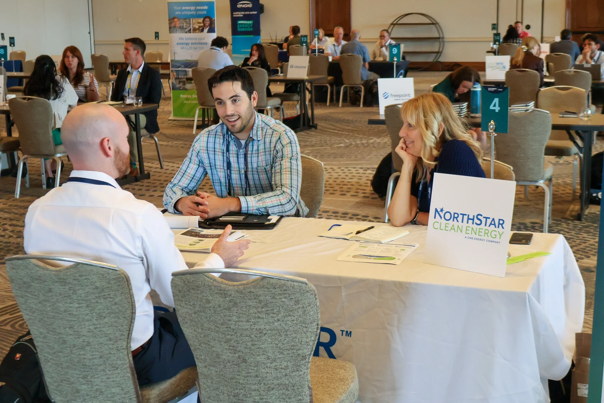 Three people seated at a table in a conference or trade show, engaged in a discussion. The table has promotional materials and a sign for NorthStar Clean Energy.