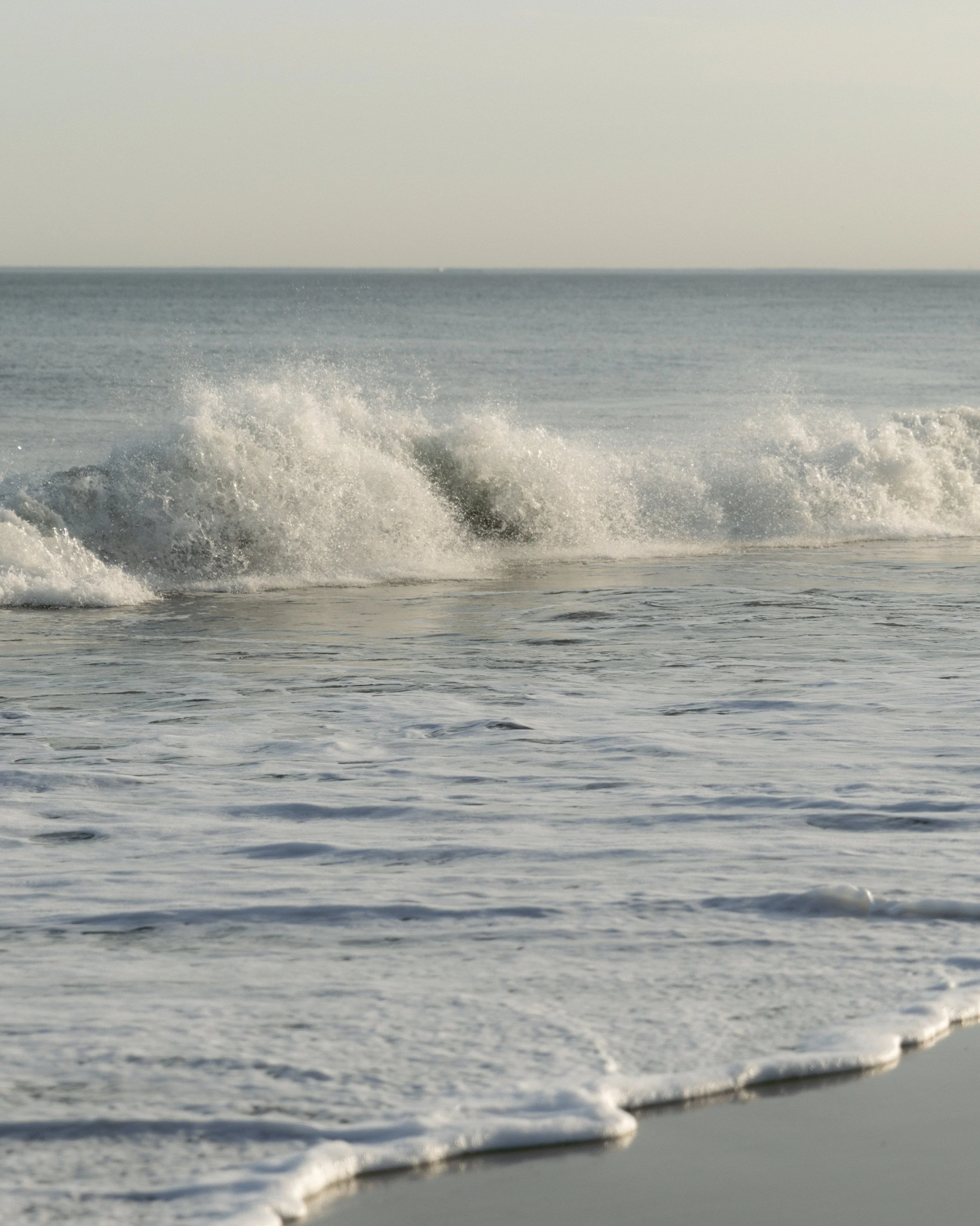 Waves crashing on a sandy beach with the ocean extending to the horizon.