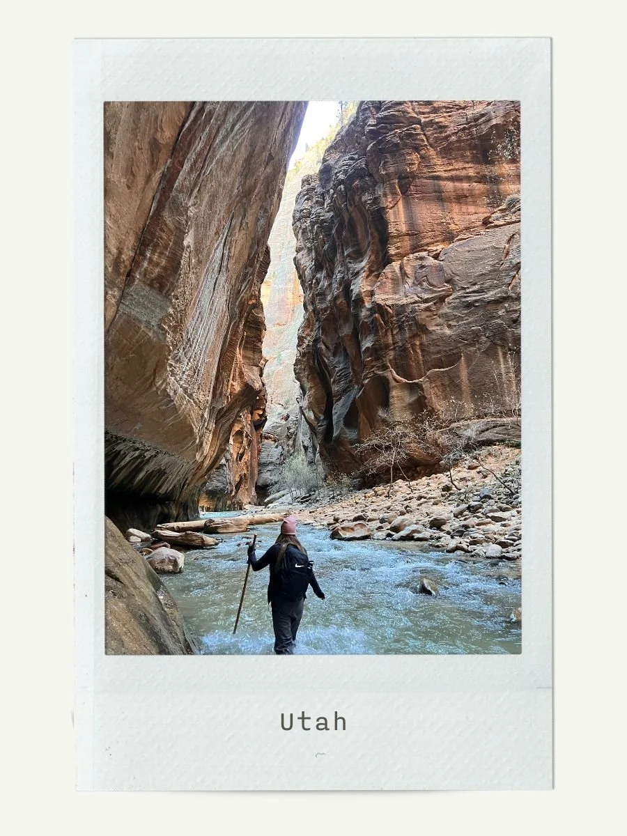 A person hiking through a narrow canyon with steep, layered rock walls and a flowing river in Utah.