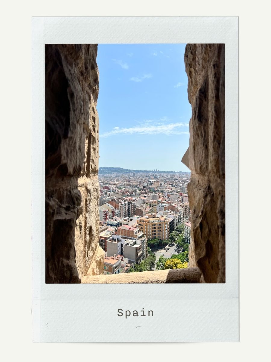 View of a cityscape through a stone window opening in Spain, with buildings, trees, and a blue sky.