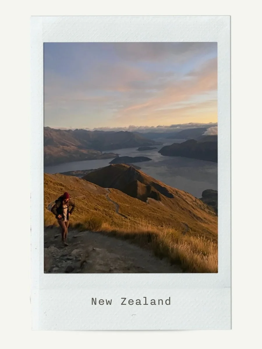 Hiker walking along a mountain trail in New Zealand with a lake in the background during sunset.