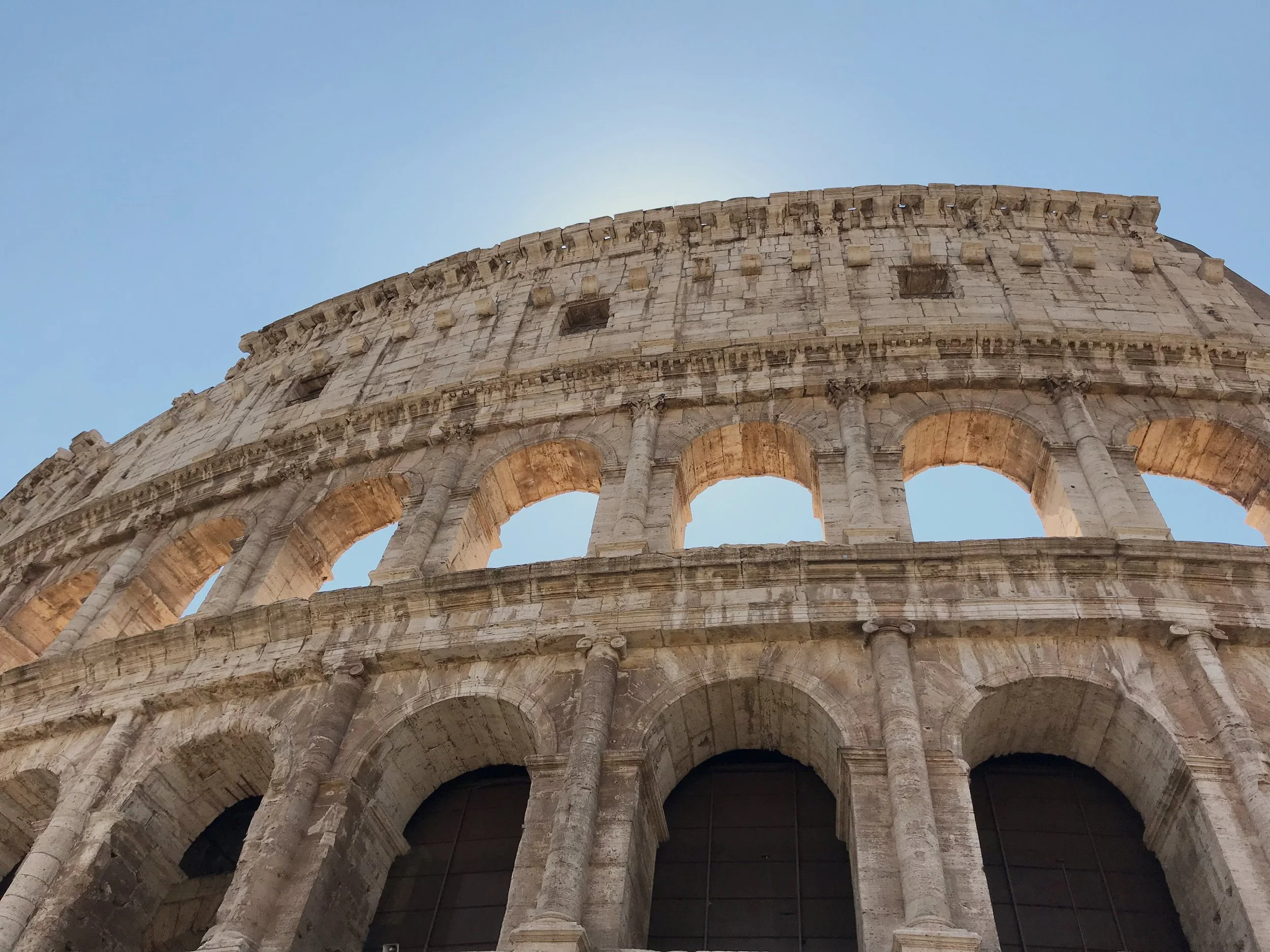 Close-up of the outer wall of the Colosseum in Rome, Italy, showing arches and stonework against a clear blue sky.