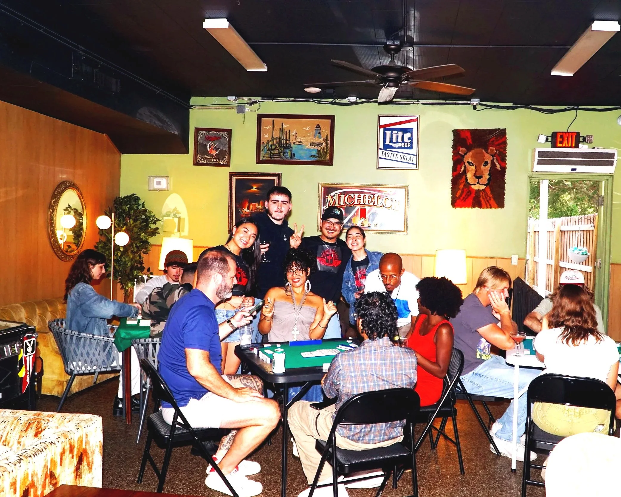 Group of people gathered around a poker table in a cozy, decorated restaurant or bar, smiling and socializing.