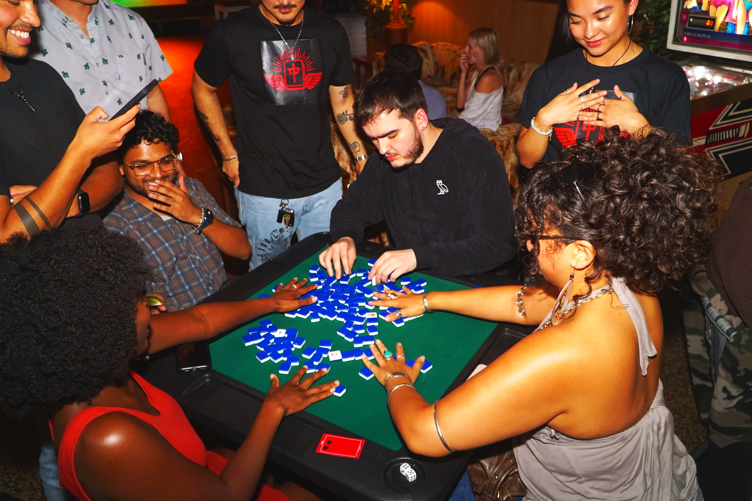 Group of people gathered around a table playing a game with blue tiles.