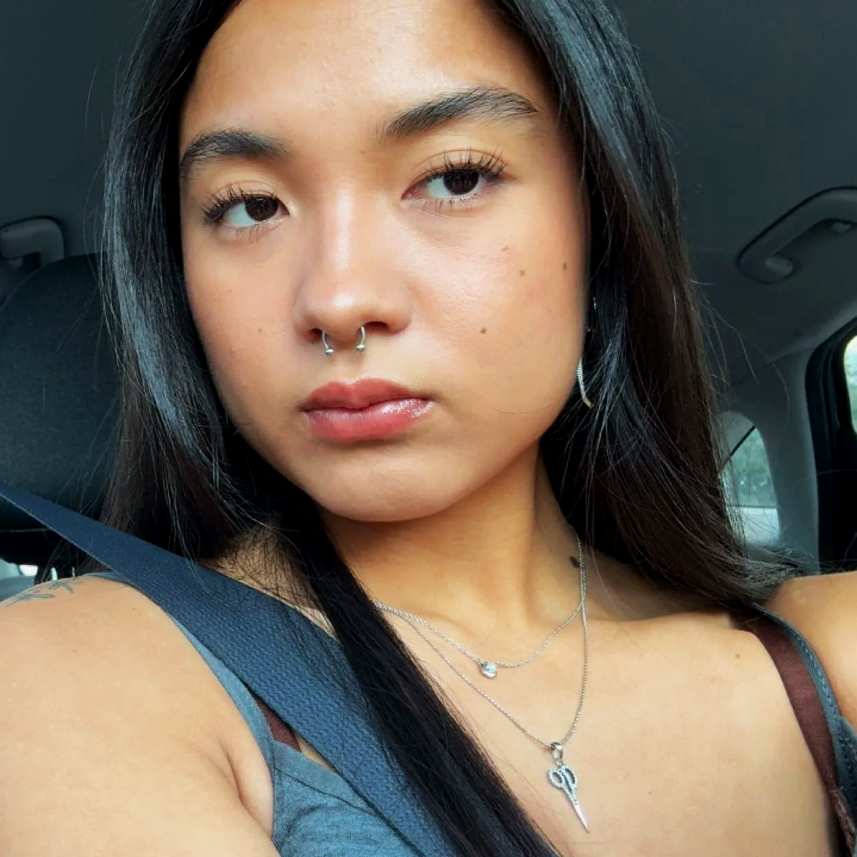 A woman with shoulder-length black hair smiling outdoors, surrounded by green plants.