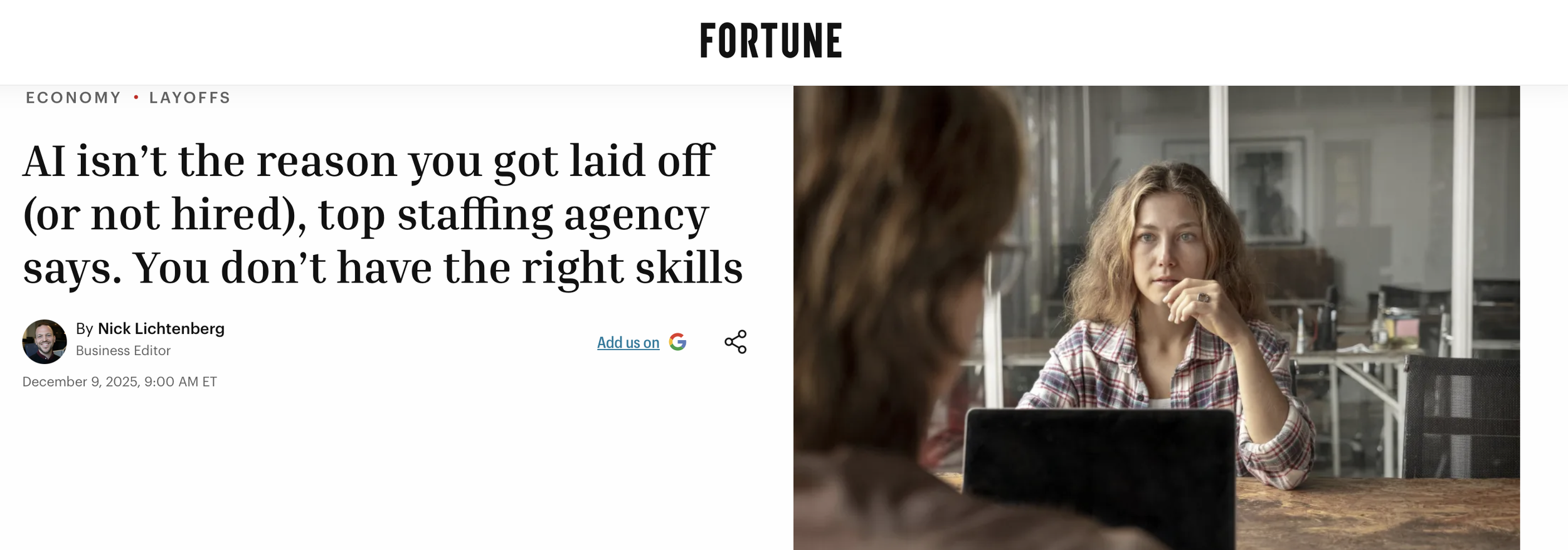 A woman with curly hair and a checkered shirt sitting inside a modern office, looking at another woman across a table, who is partially visible.