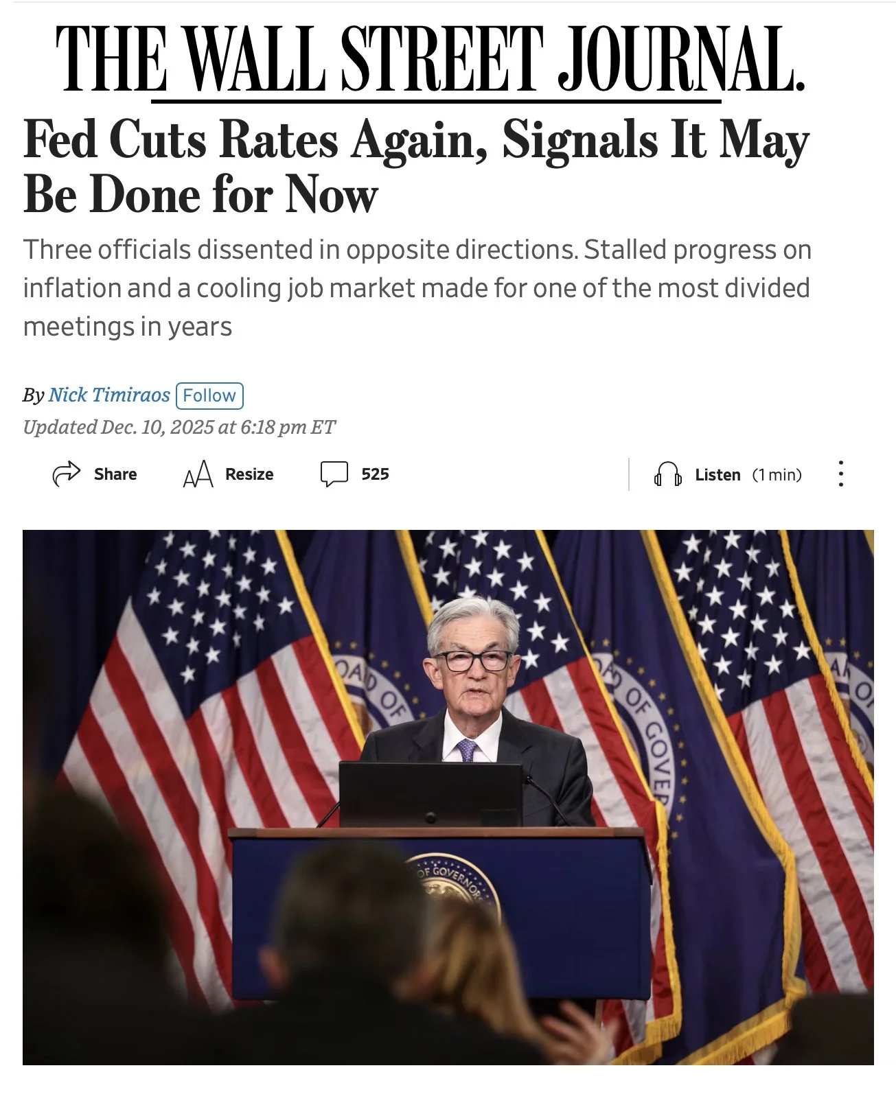 A man in a suit and glasses standing at a podium with multiple American flags in the background.