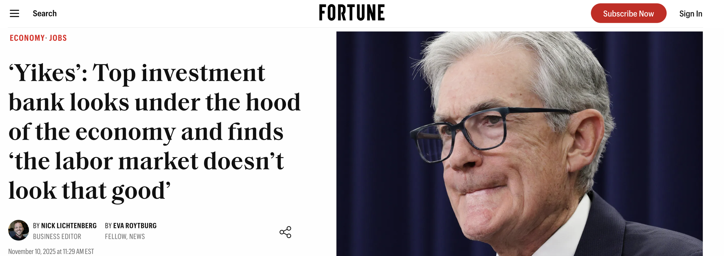 Close-up of an older man with gray hair and glasses smiling, wearing a dark suit and white shirt.