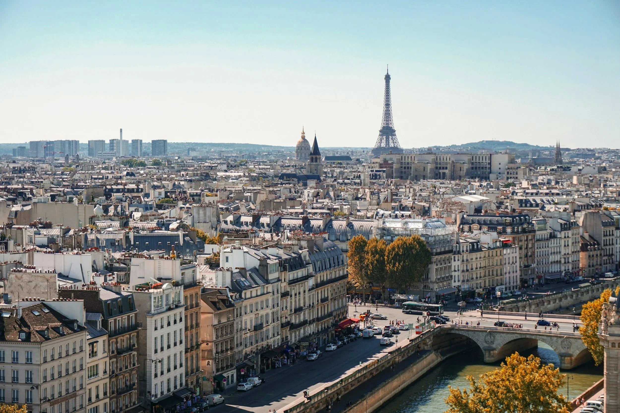 Vue panoramique de Paris avec la tour Eiffel en arrière-plan, les bâtiments traditionnels et la Seine au premier plan.