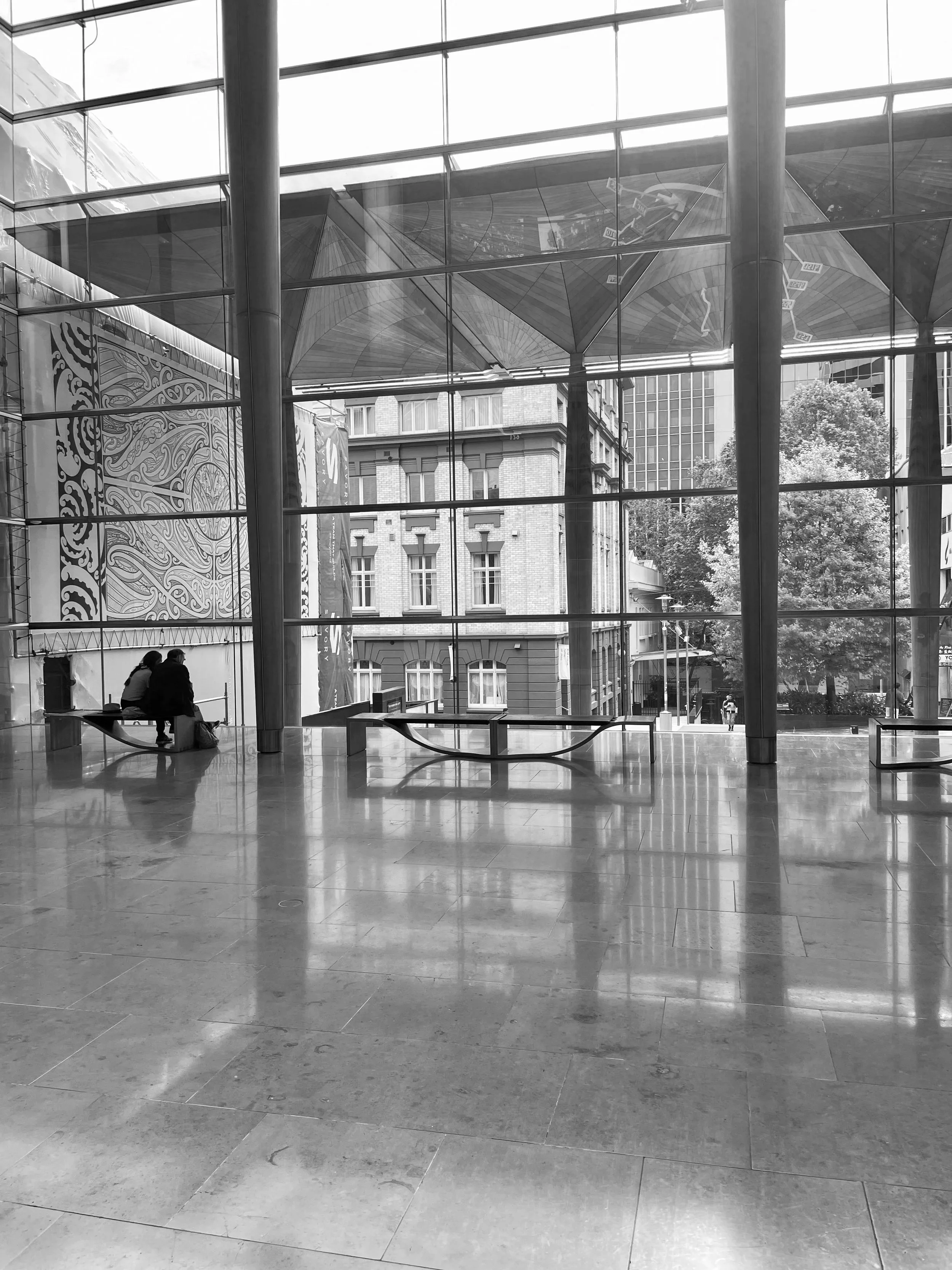 A couple sitting at Auckland Art Gallery facing the big glass window