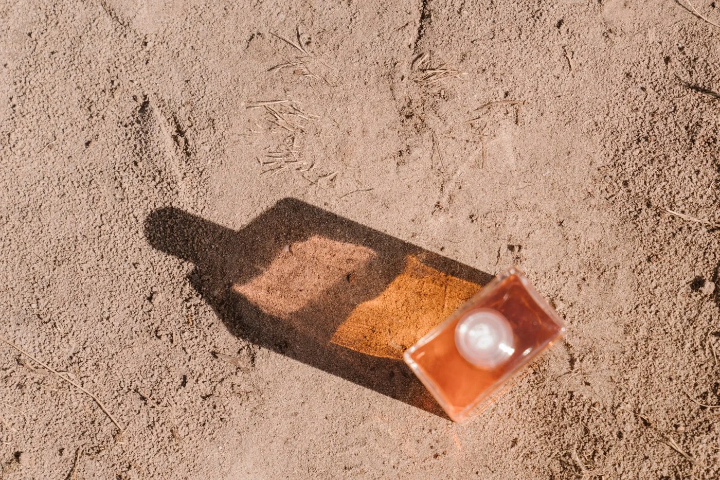 Aura-Soma fles met eigen schaduw op een ondergrond van zand