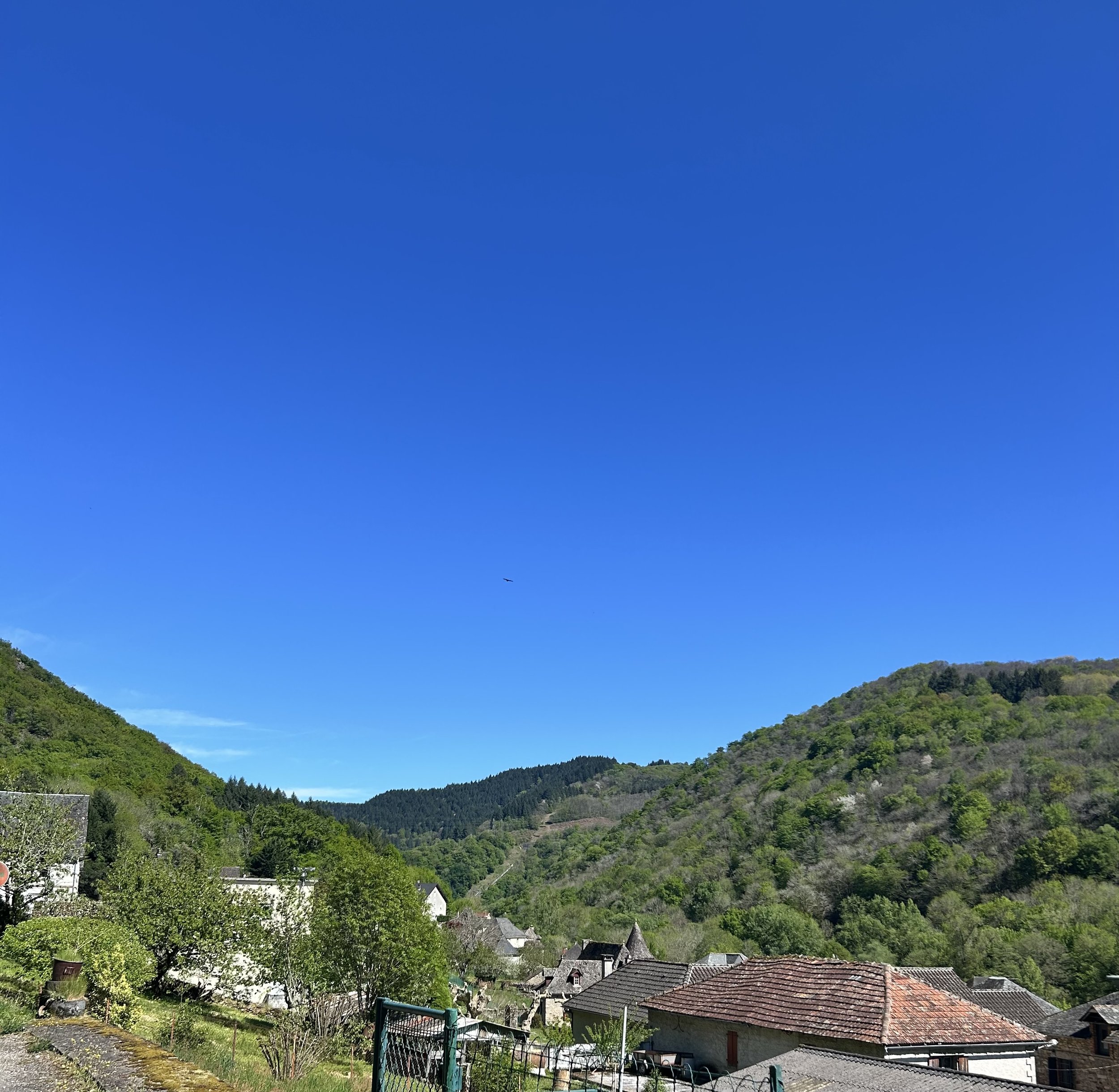 A scenic view of a rural village with rooftops and lush green hills under a clear blue sky.
