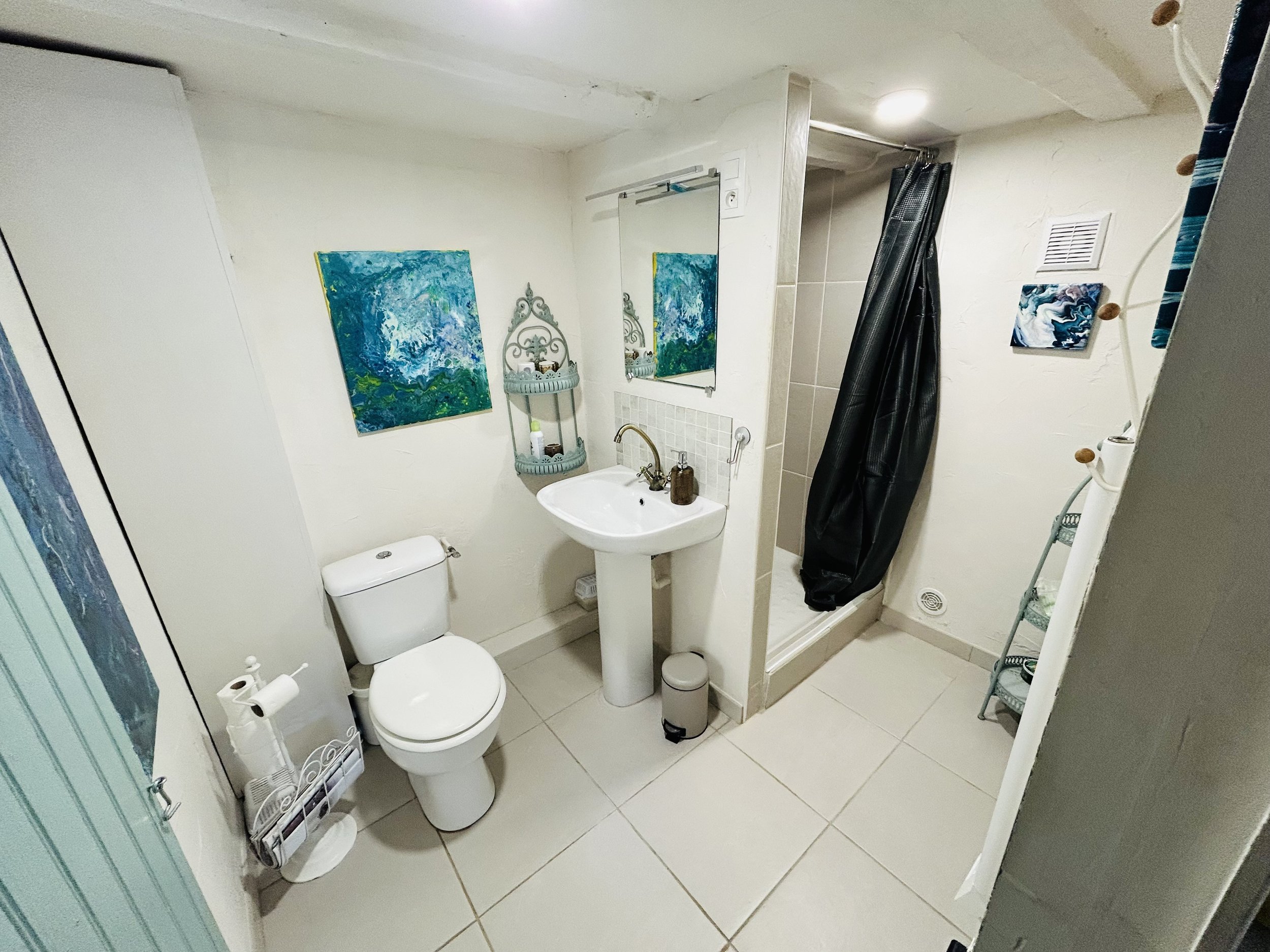 Small bathroom with a toilet, pedestal sink, shower with a dark curtain, and abstract wall art.