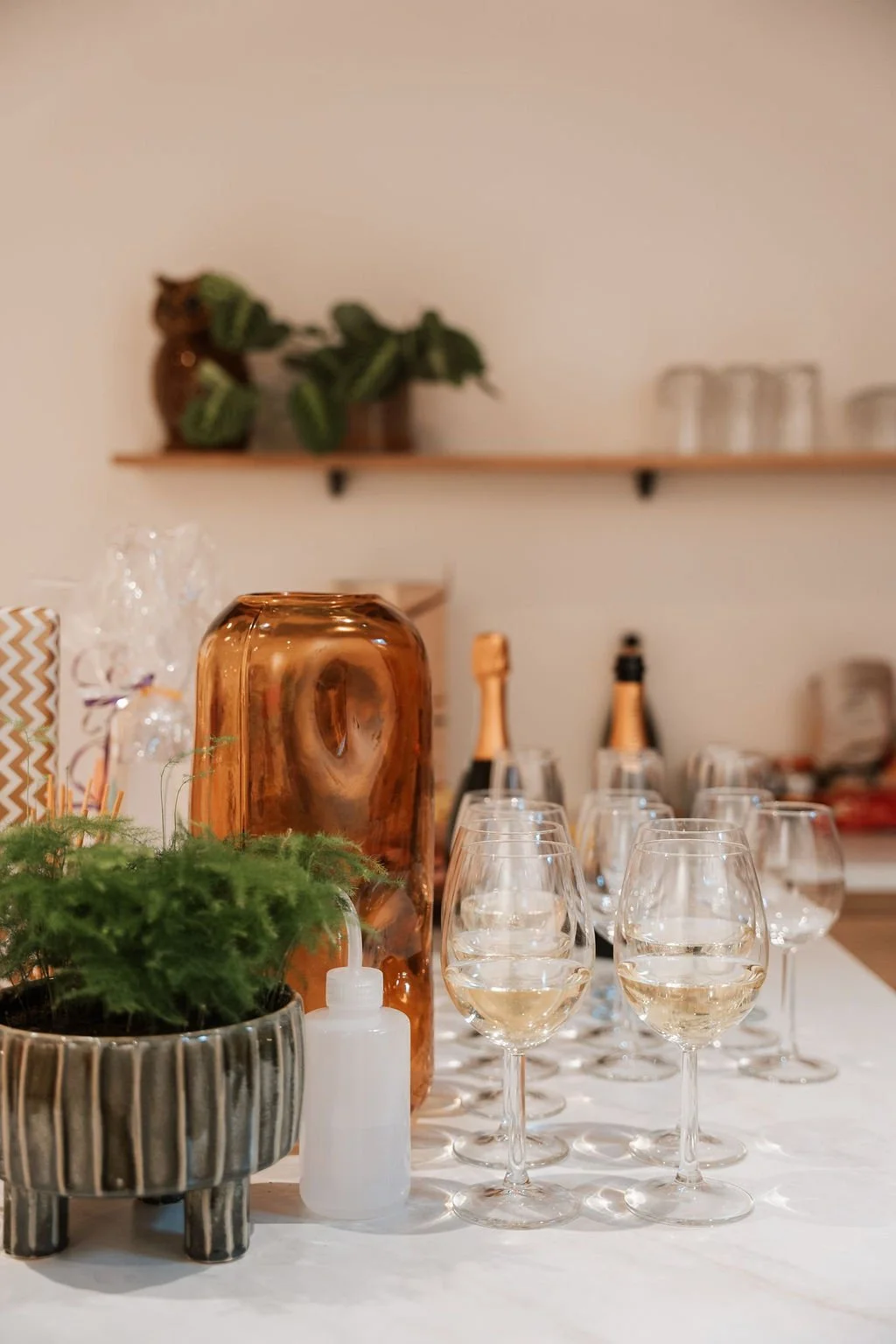 Decoratieve glazen met witte wijn, planten, champagneflessen, en huishoudelijke artikelen op een tafel.