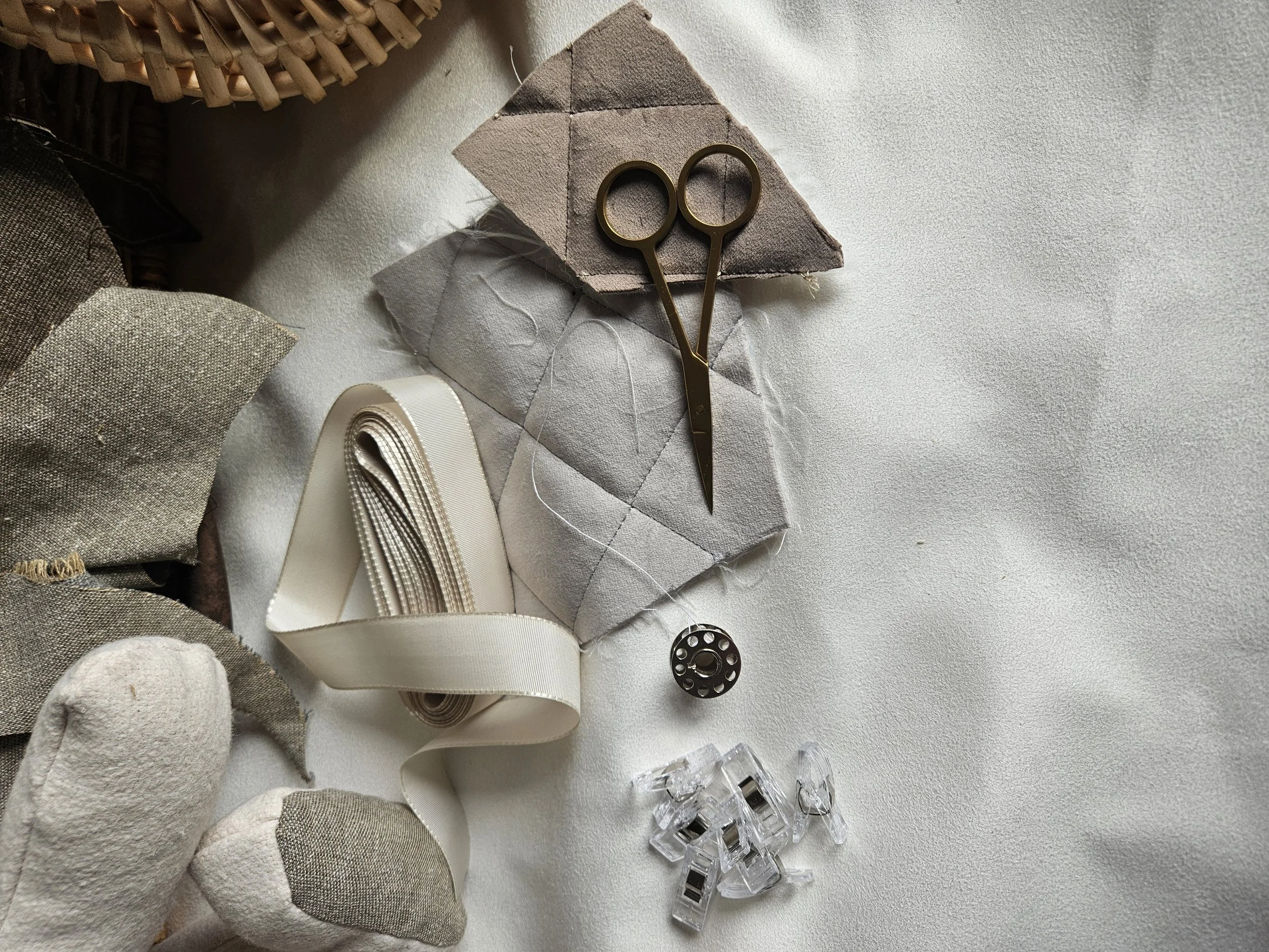 Sewing supplies including scissors, fabric pieces, ribbon, a bobbin, and clips arranged on a white surface.
