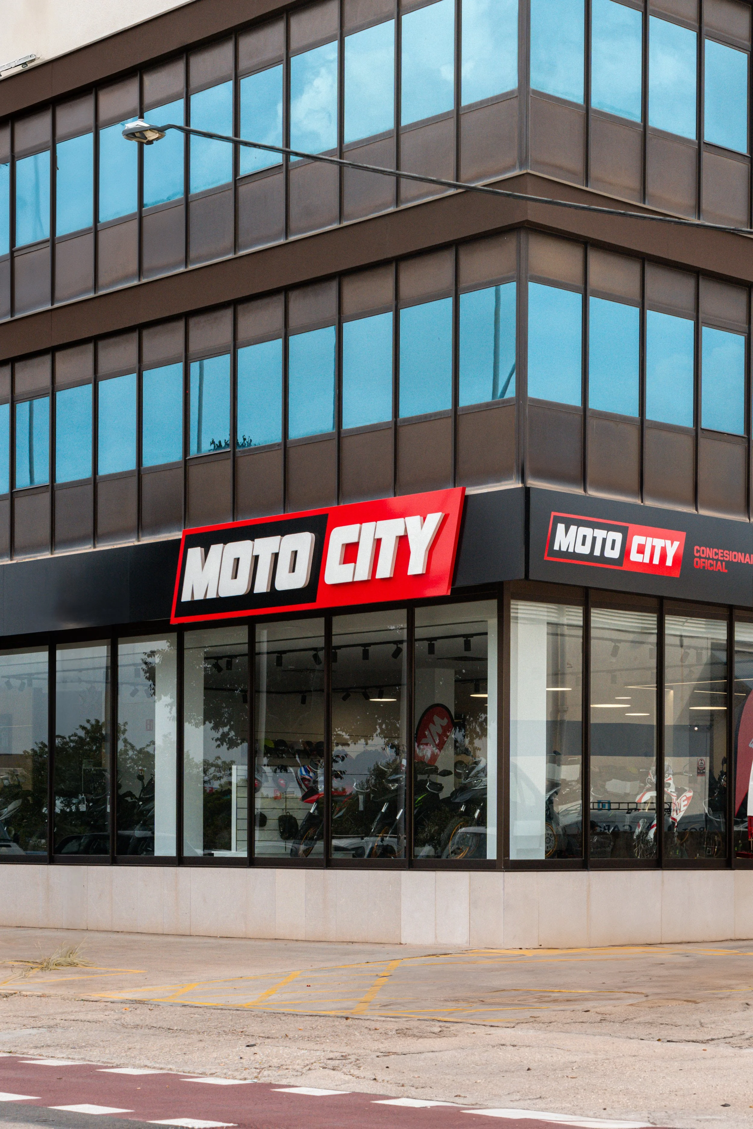 Vista exterior de un edificio con cristaleras y un cartel que dice 'MOTO CITY', un concesionario de motocicletas, en la esquina del edificio.
