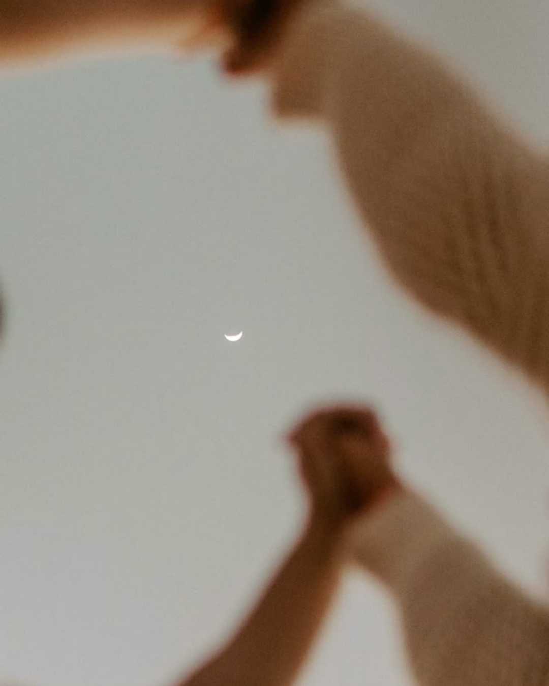 Manos en posición de oración con la luna creciente en el cielo al fondo.