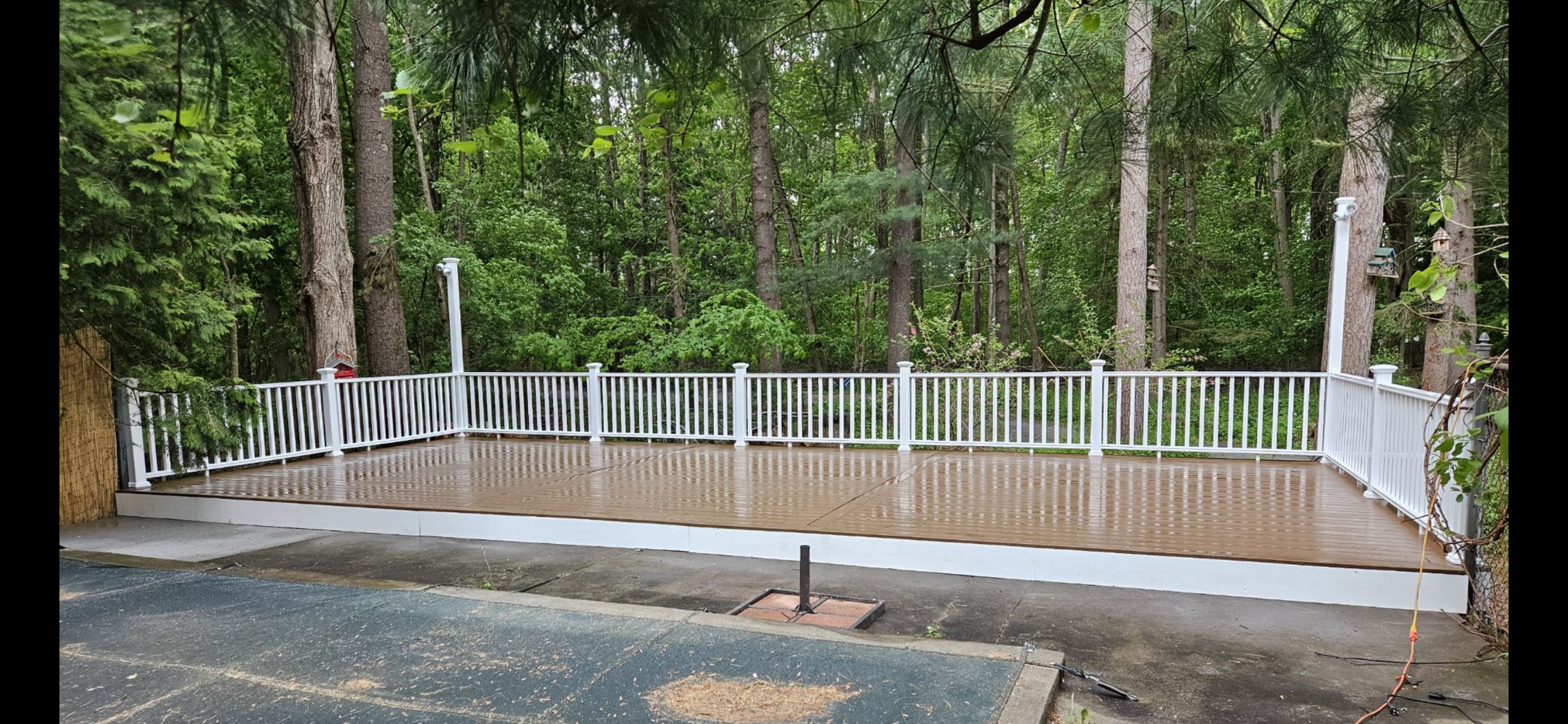 Empty wooden deck with white railing attached to a forested backyard.