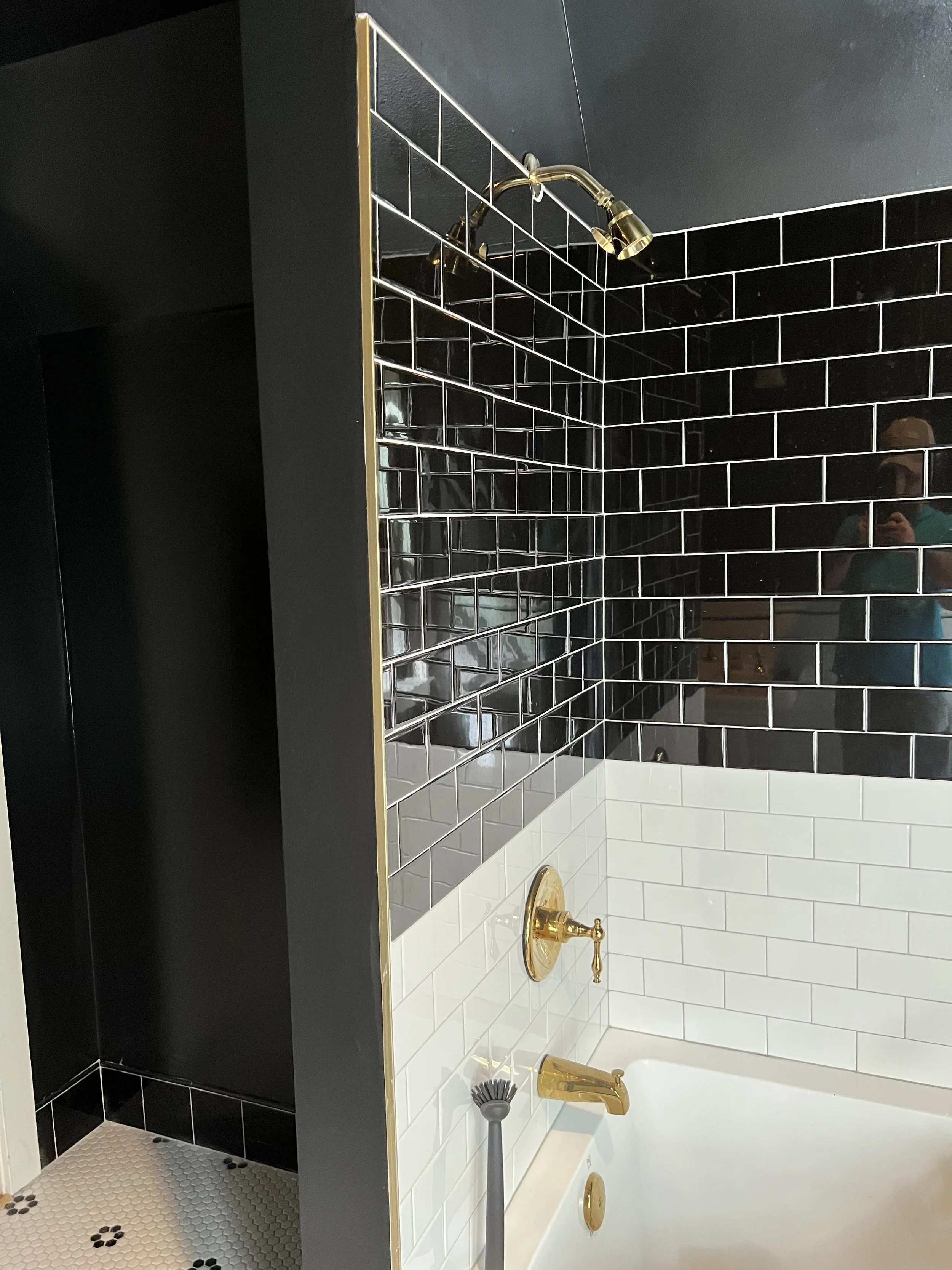Bathroom shower with black subway tiles, white tiles around the tub, and gold fixtures.