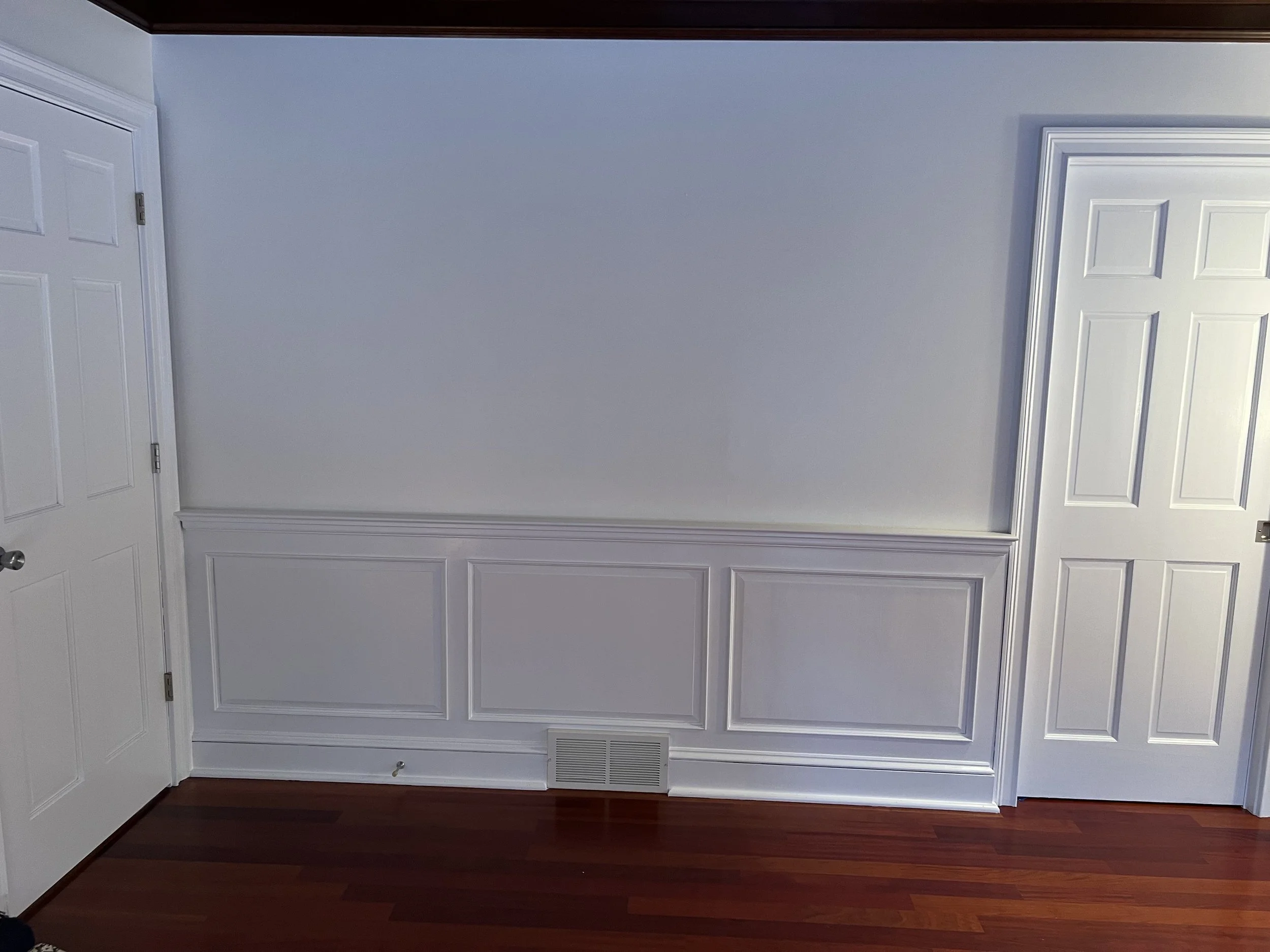 Interior wall with white wainscoting and paneling, two closed white doors, and a hardwood floor.