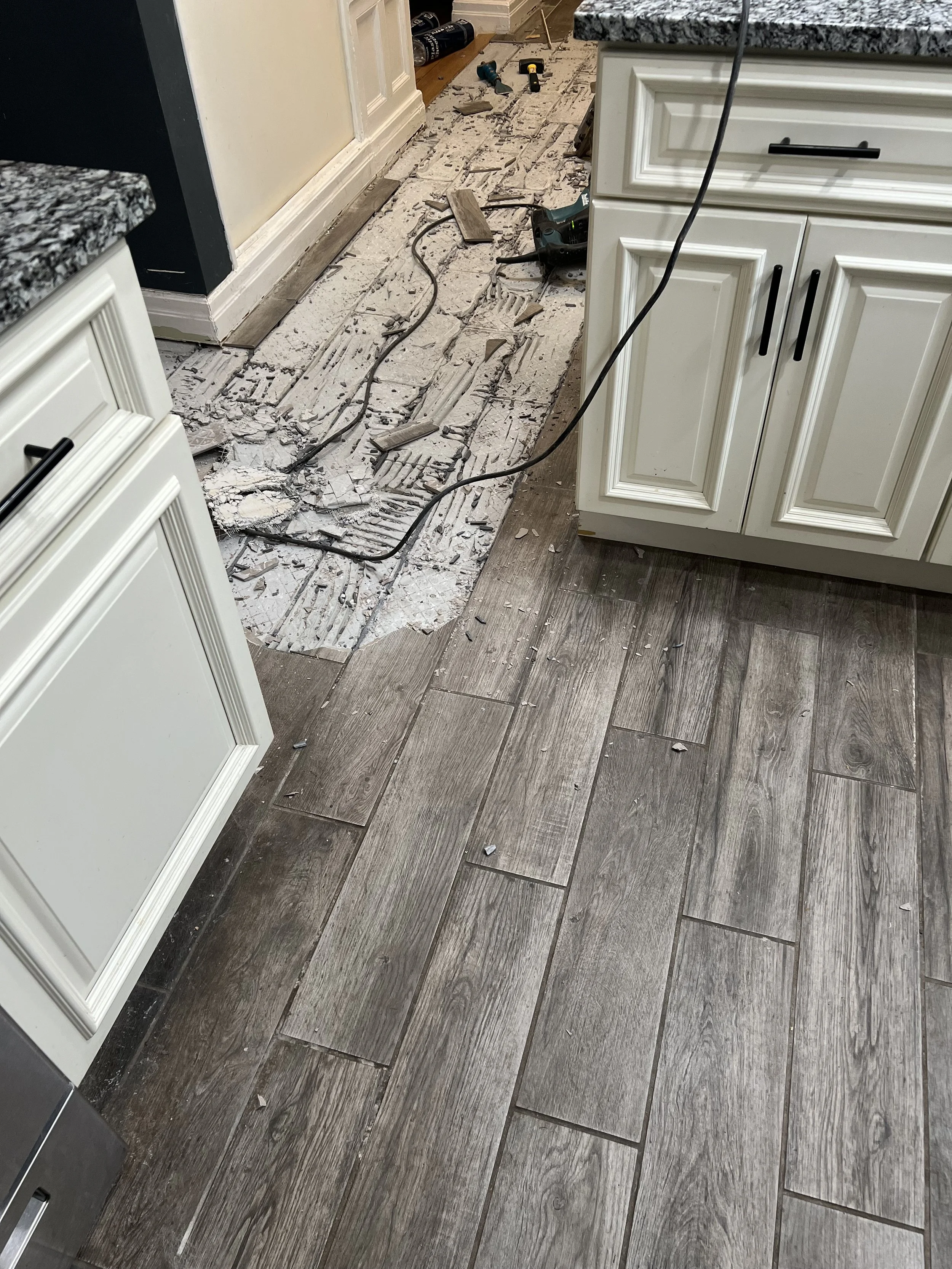Kitchen with partially removed flooring revealing subfloor and tools scattered around.