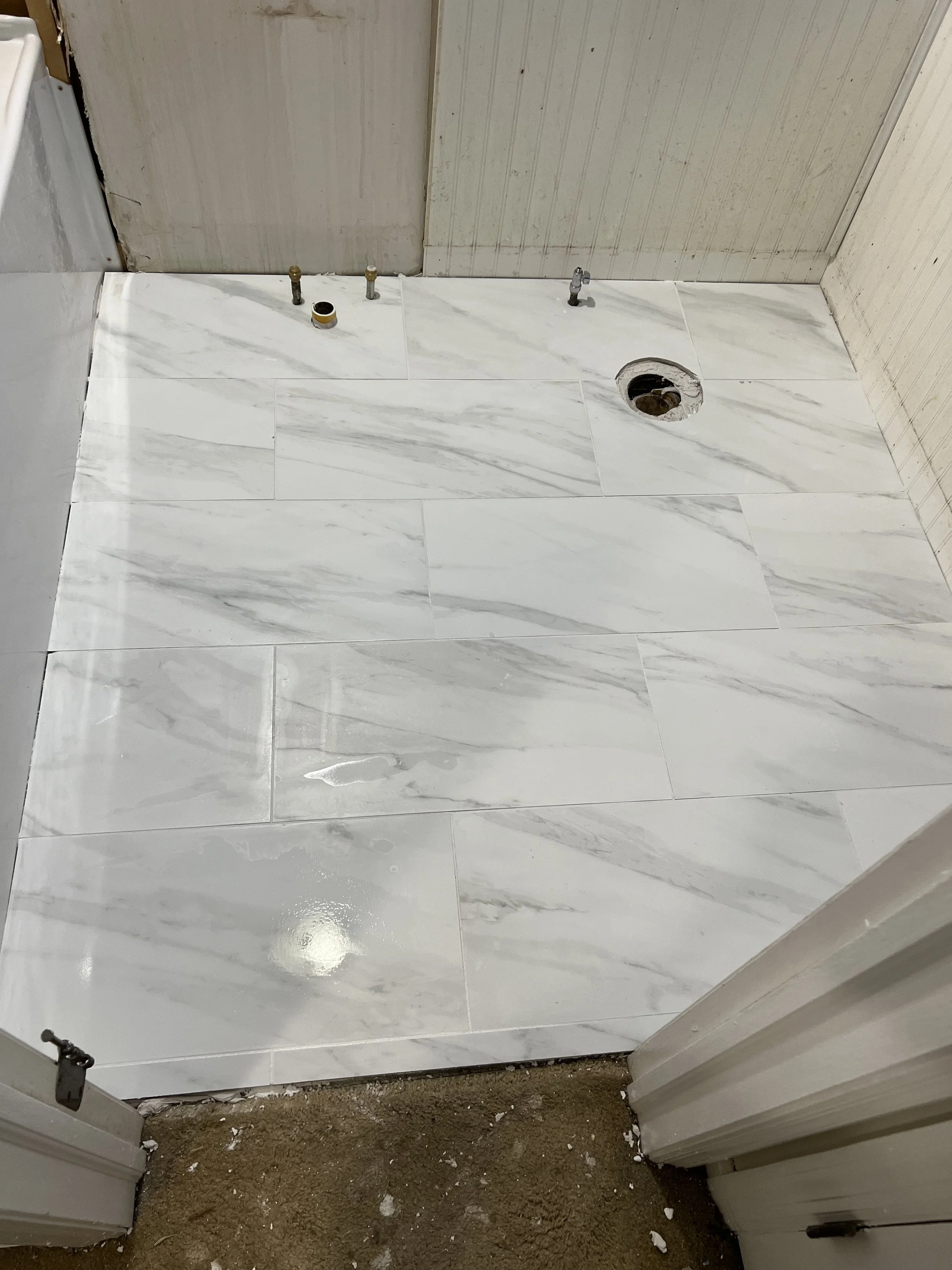 Bathroom floor with white marble tiles, plumbing fixtures, and partially constructed wall.