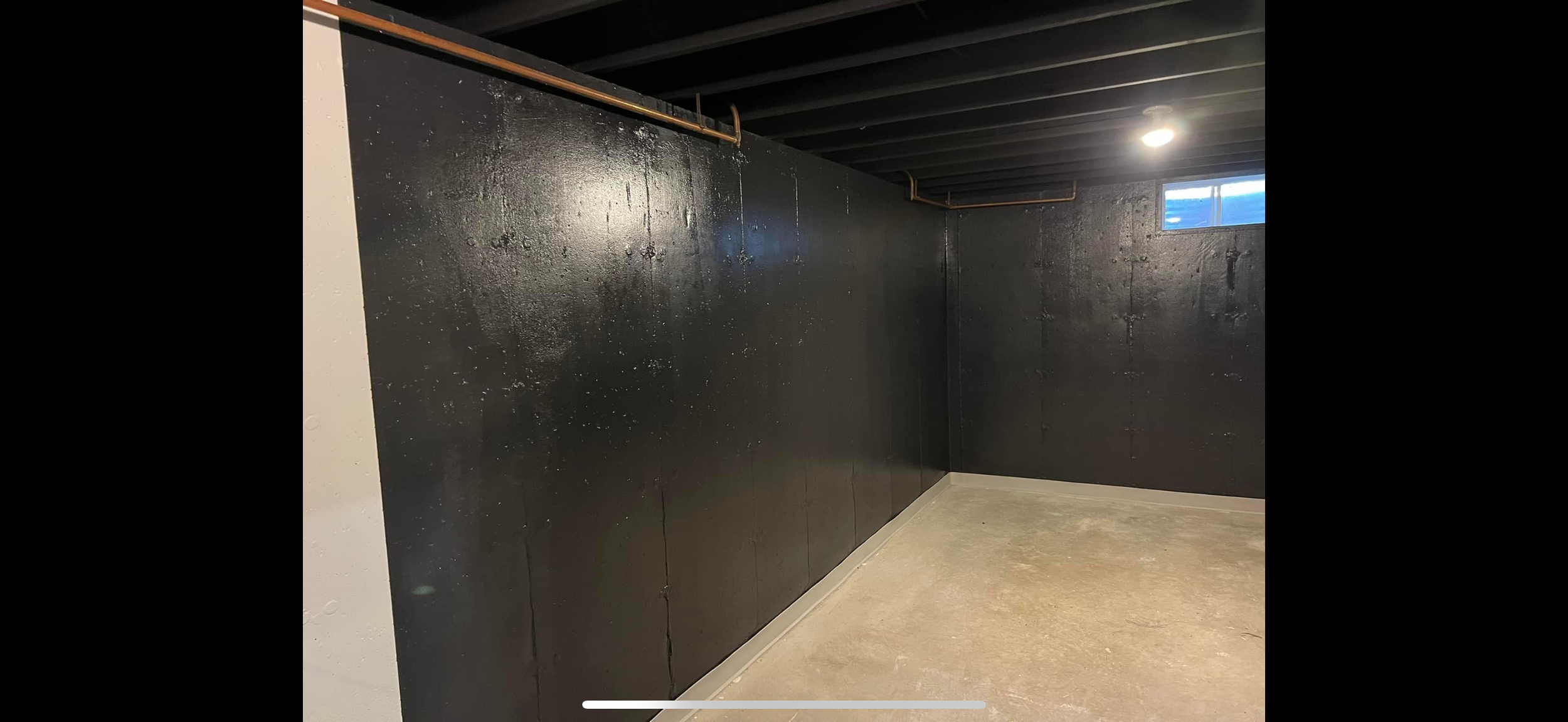 Basement with black painted walls, concrete floor, and small high window, illuminated by ceiling light.