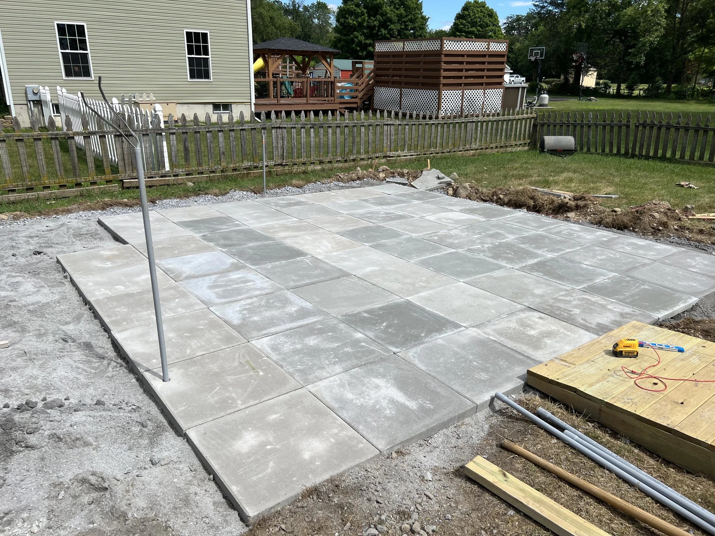 Newly paved concrete patio being constructed in a backyard, with construction tools and materials nearby.
