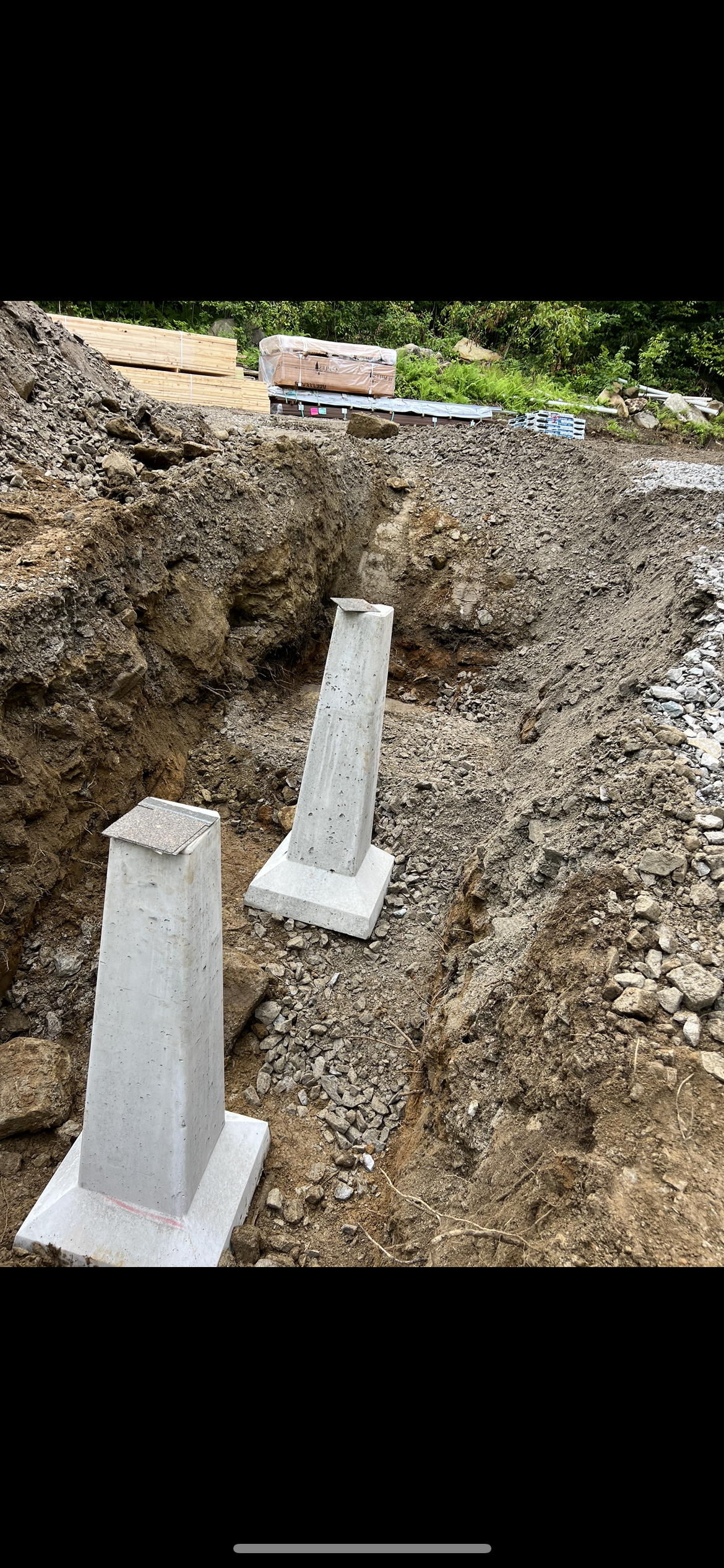 Construction site showing an excavated trench with two concrete supports.