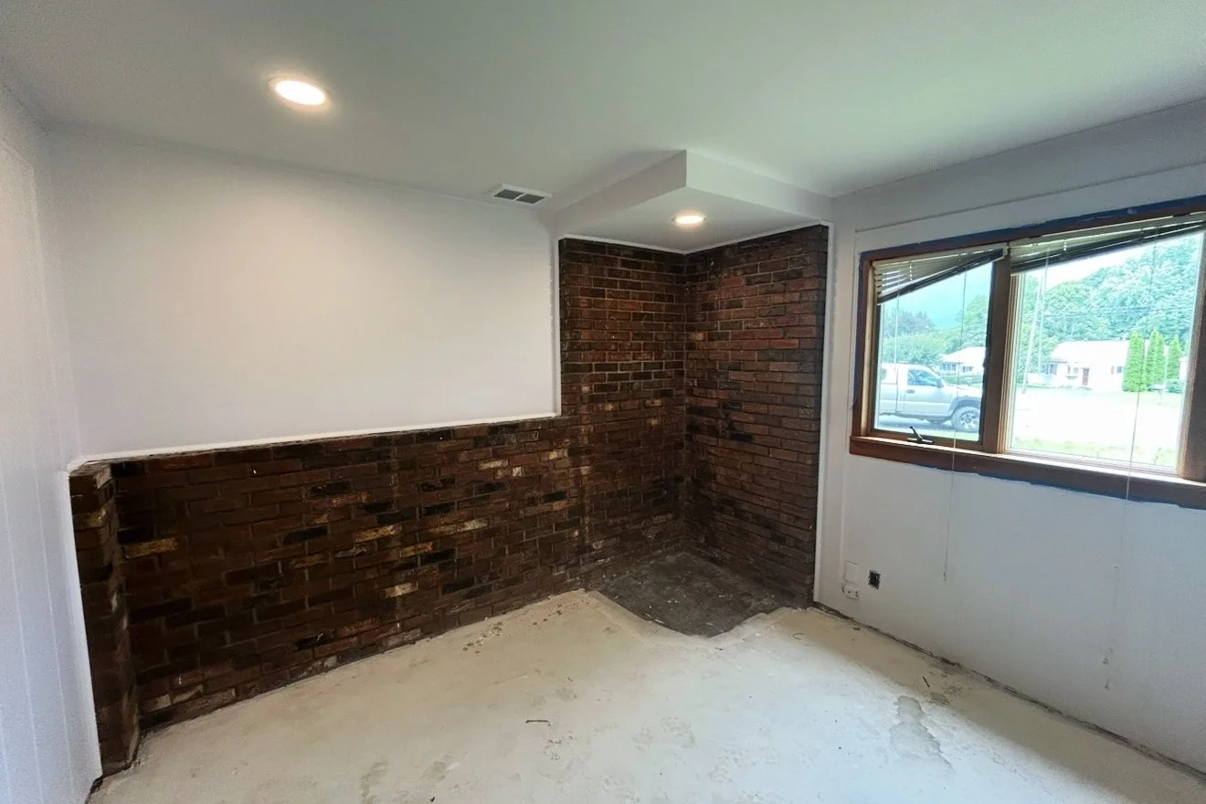 Room with white walls, brick accents, a window with blinds, and a partially visible ceiling light.