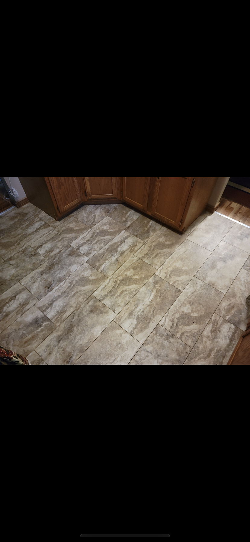 Tile flooring in a kitchen with wooden cabinets at the bottom of the image.