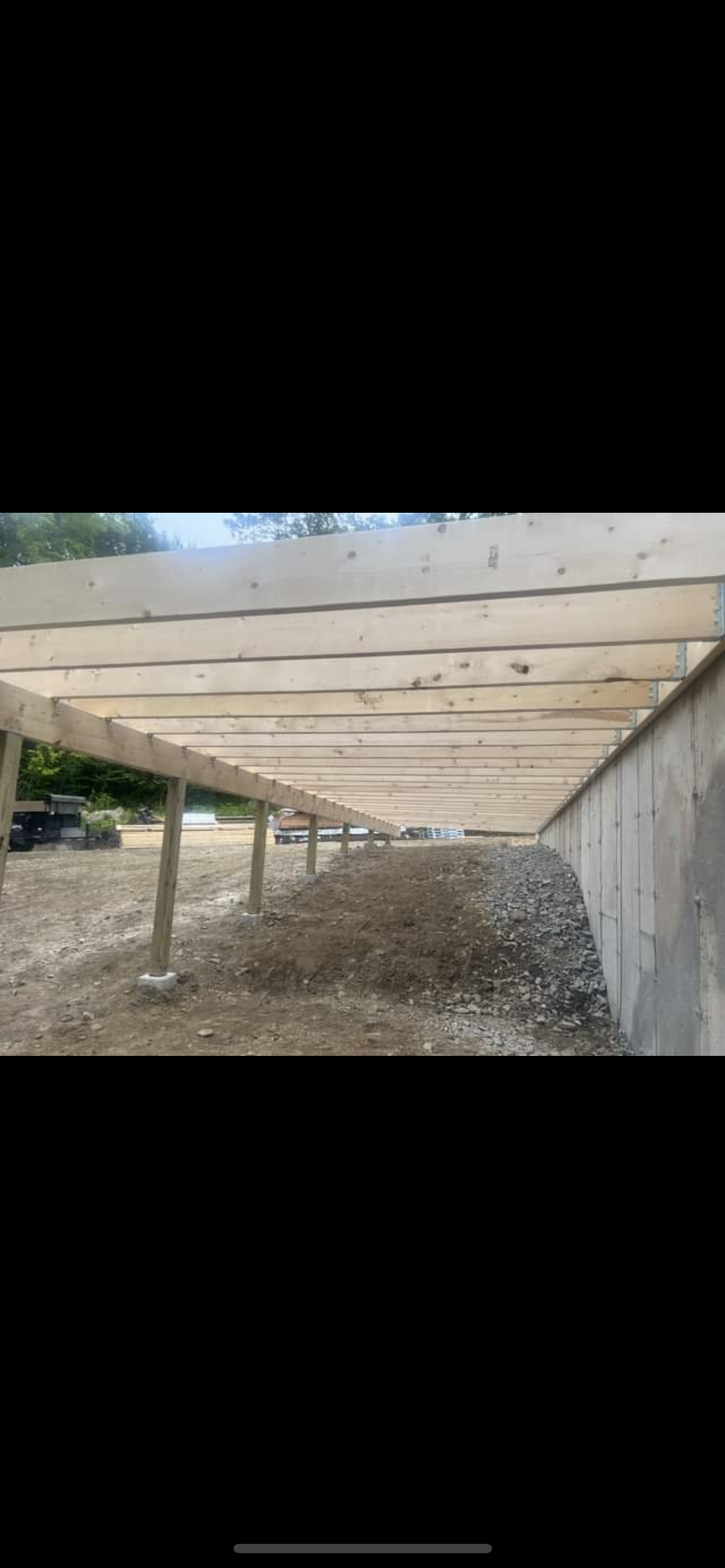 Under construction wooden support beams for a building or bridge, with soil and gravel ground underneath.