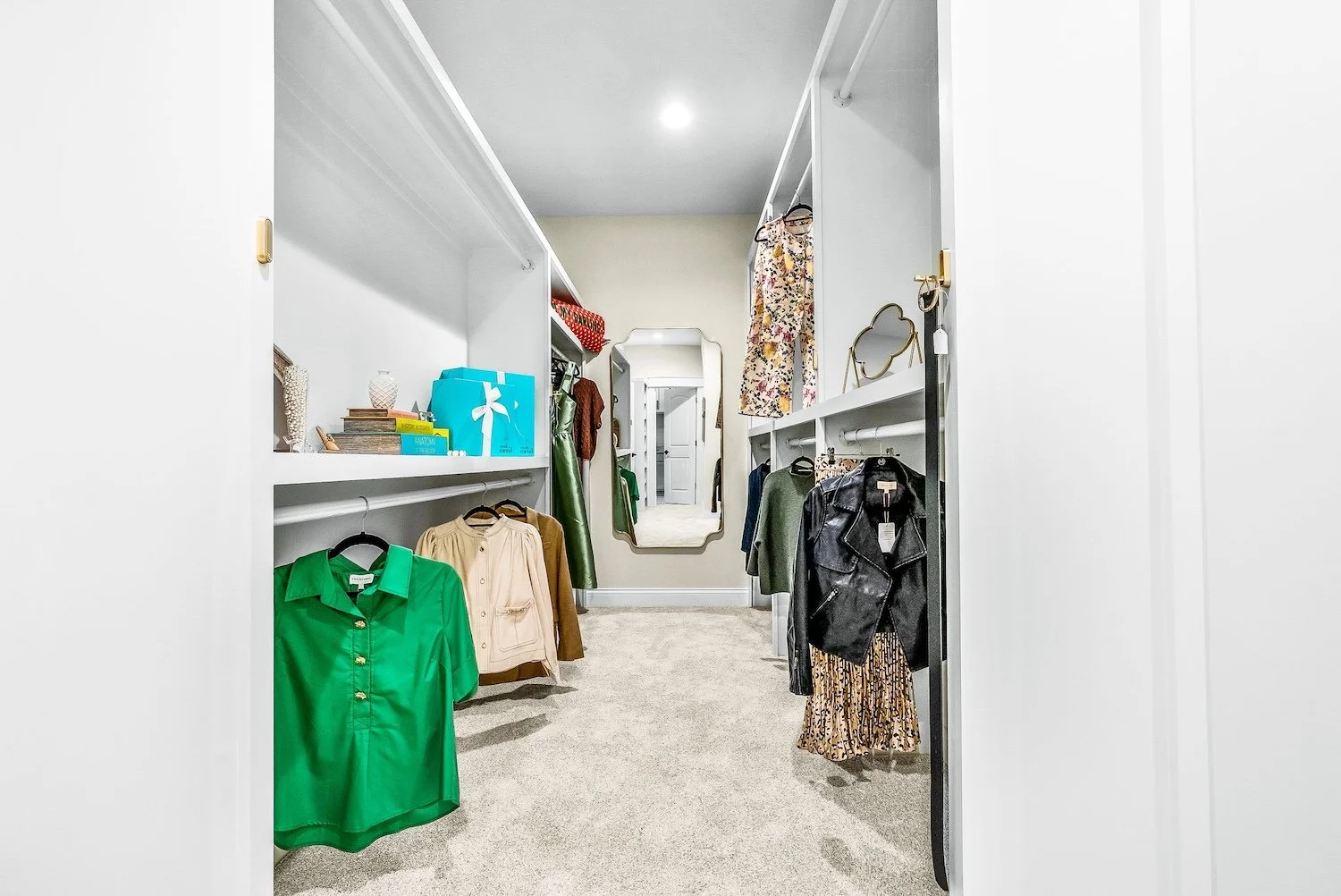 Walk-in closet with shelves and hanging rods filled with clothes, a full-length mirror, and decorative accessories.