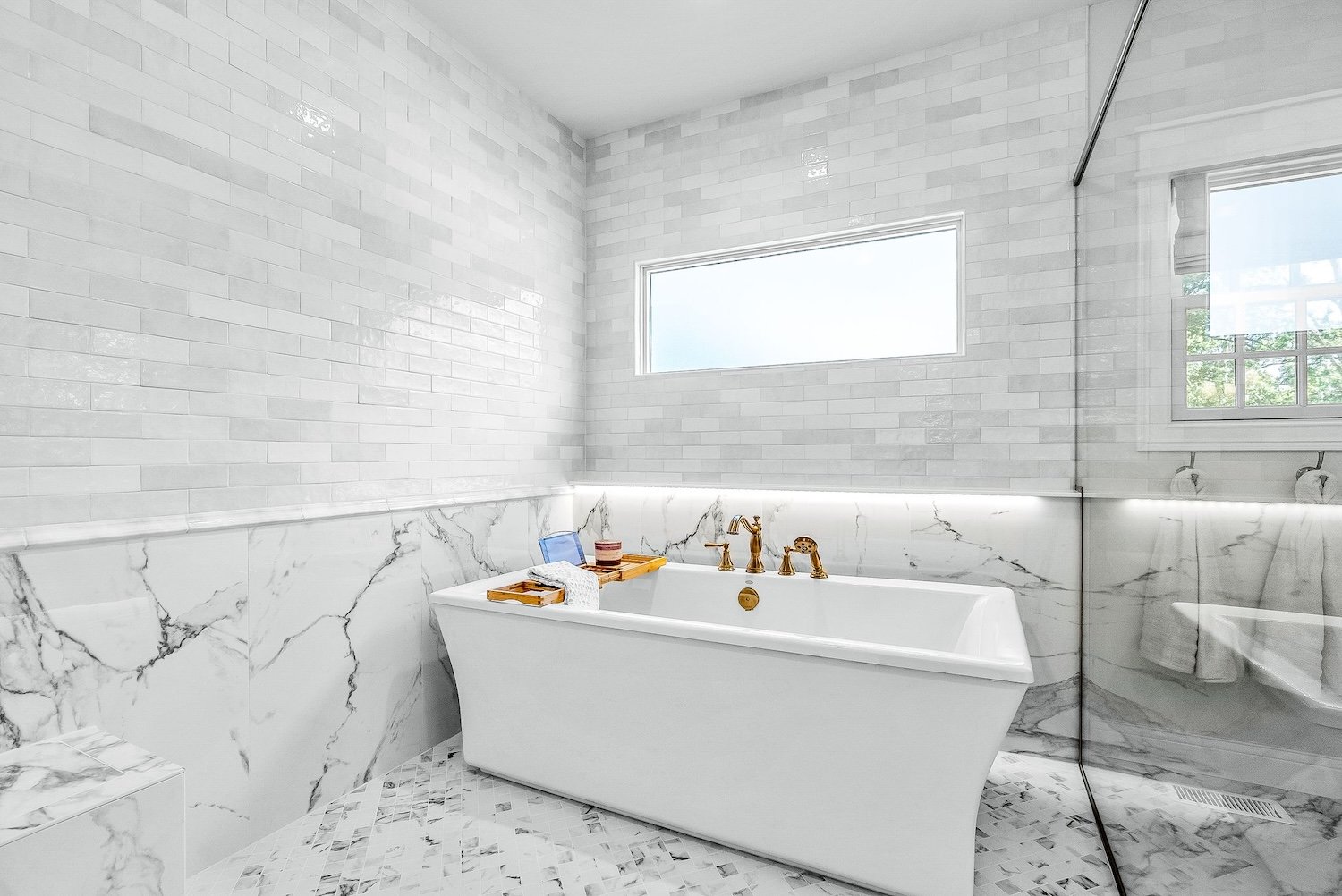 White modern bathroom with a freestanding bathtub, marble tile accents, and a large window letting in natural light.