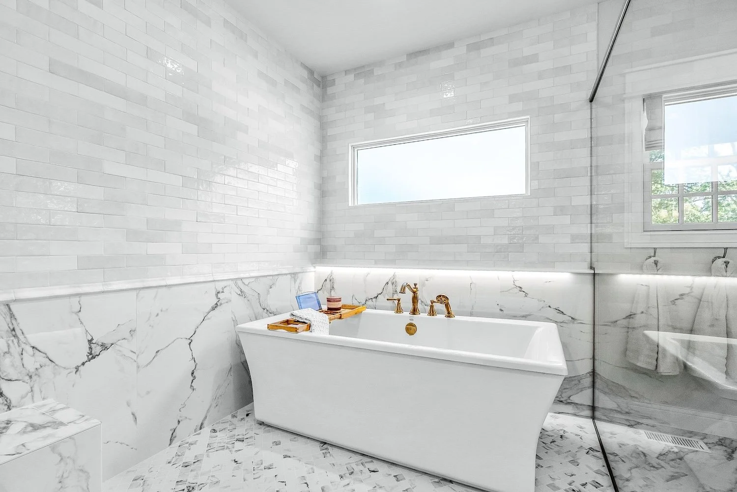 White modern bathroom with a freestanding bathtub, marble tile accents, and a large window letting in natural light.