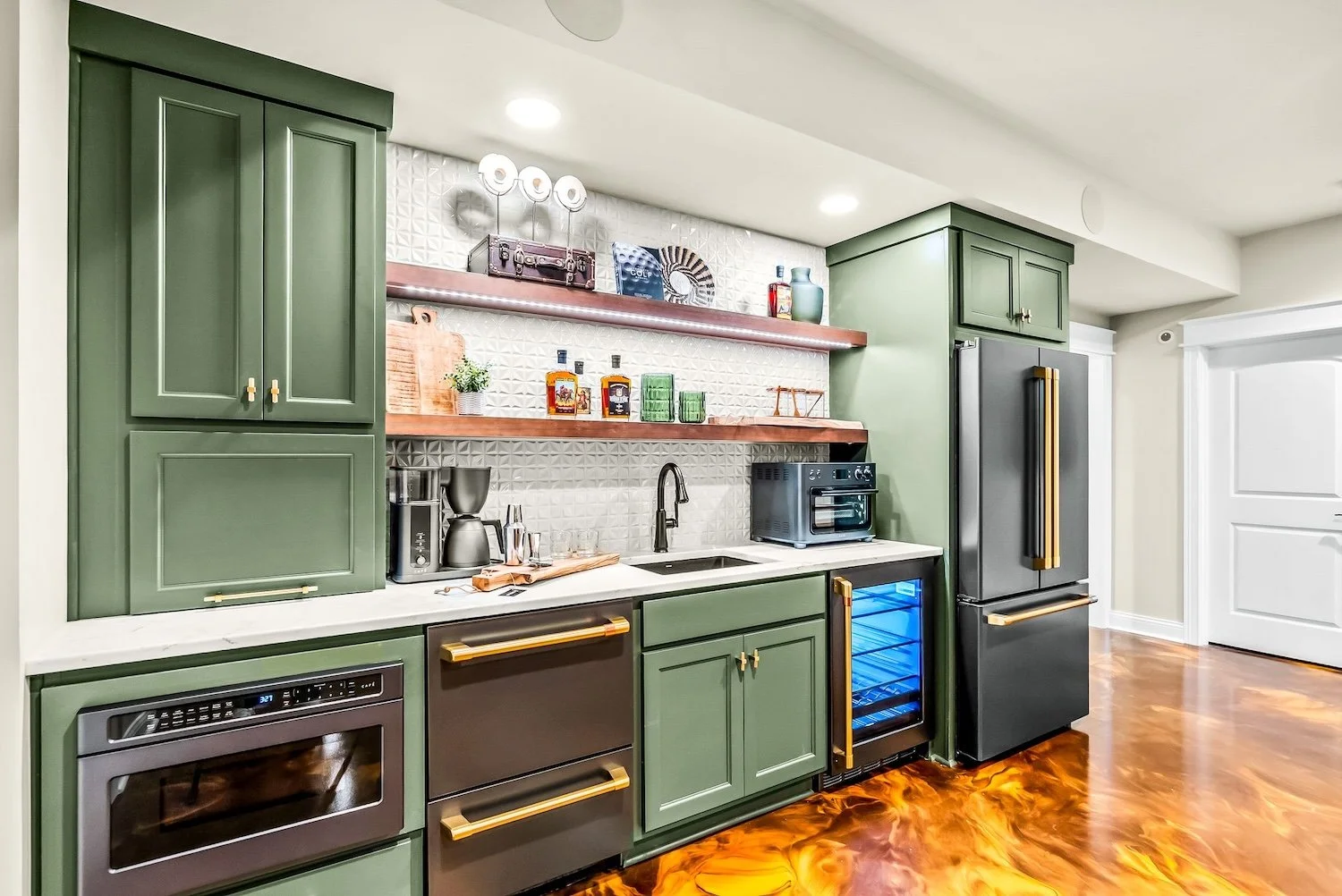 Modern kitchen with green cabinets, black appliances, open wooden shelves, and a textured white tile backsplash.