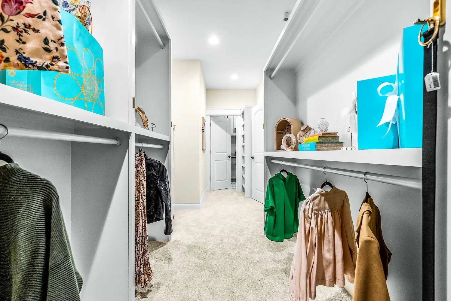 Walk-in closet with hanging clothes, shelves with decorative items, storage bins, and closed doors at the end of the room.