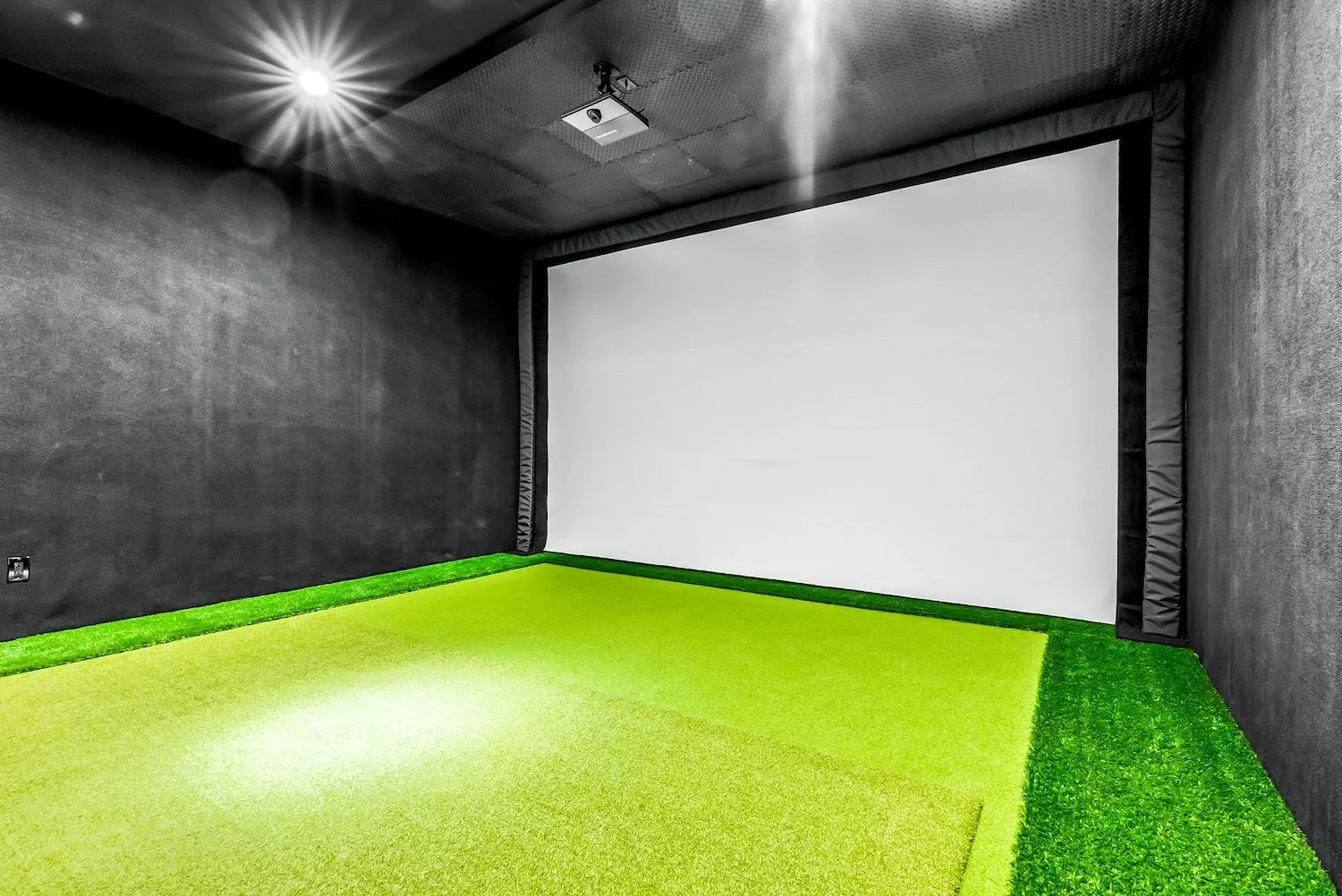 A gaming or home theater room with dark walls, a white screen, and green artificial turf flooring.