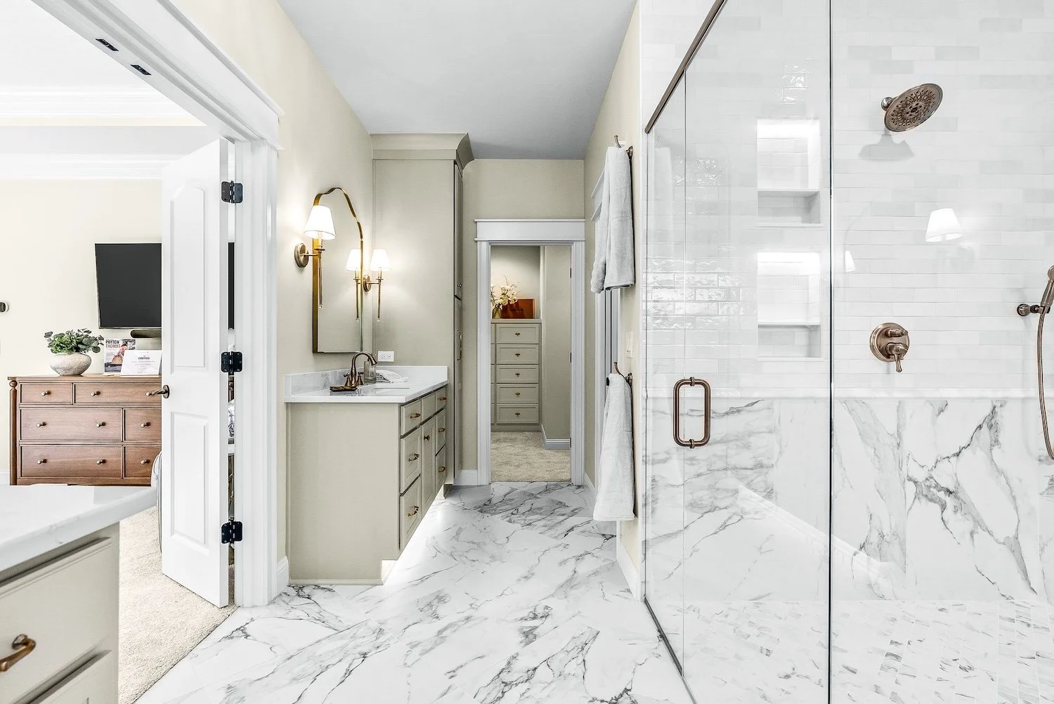 Luxurious bathroom with marble flooring and shower, beige walls, gold fixtures, and vanity with mirror
